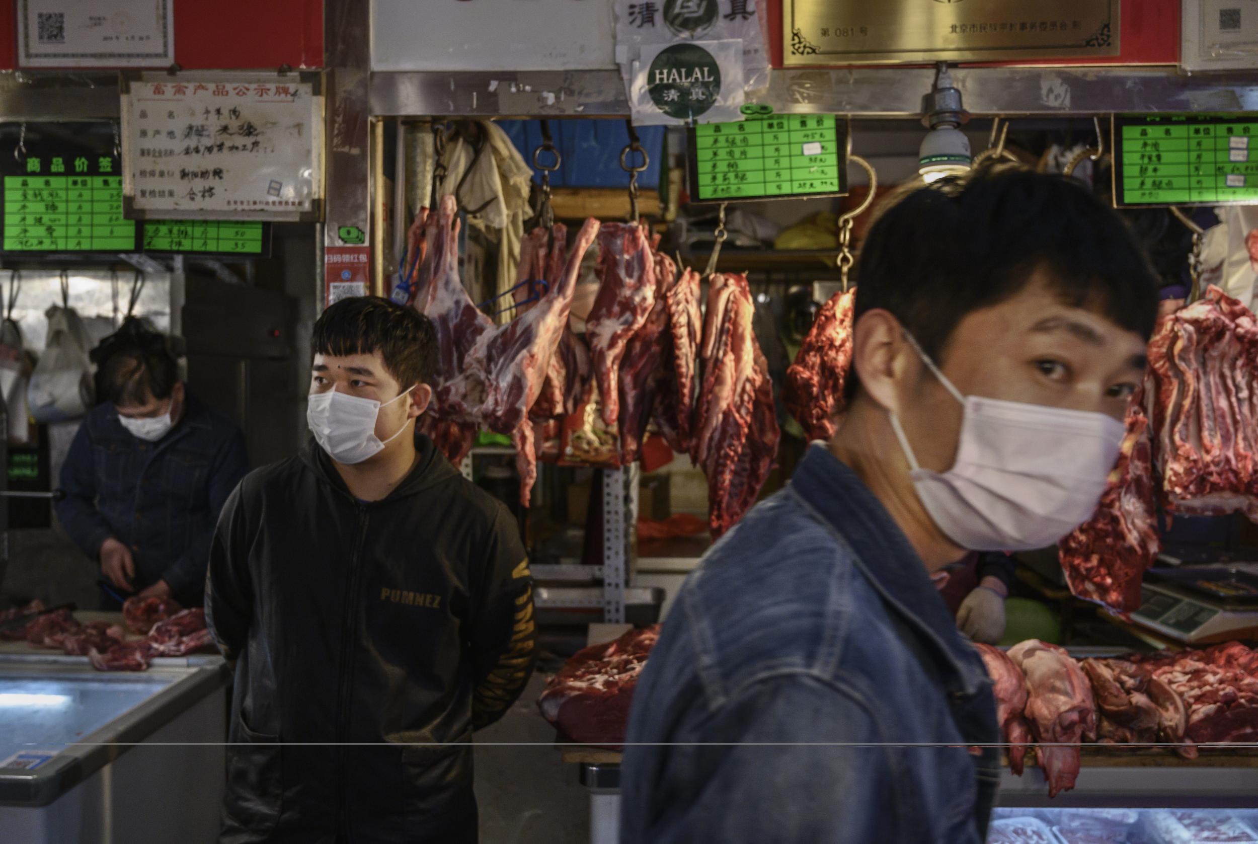 Chinese meat vendors wear protective masks as they wait for customers at a local market