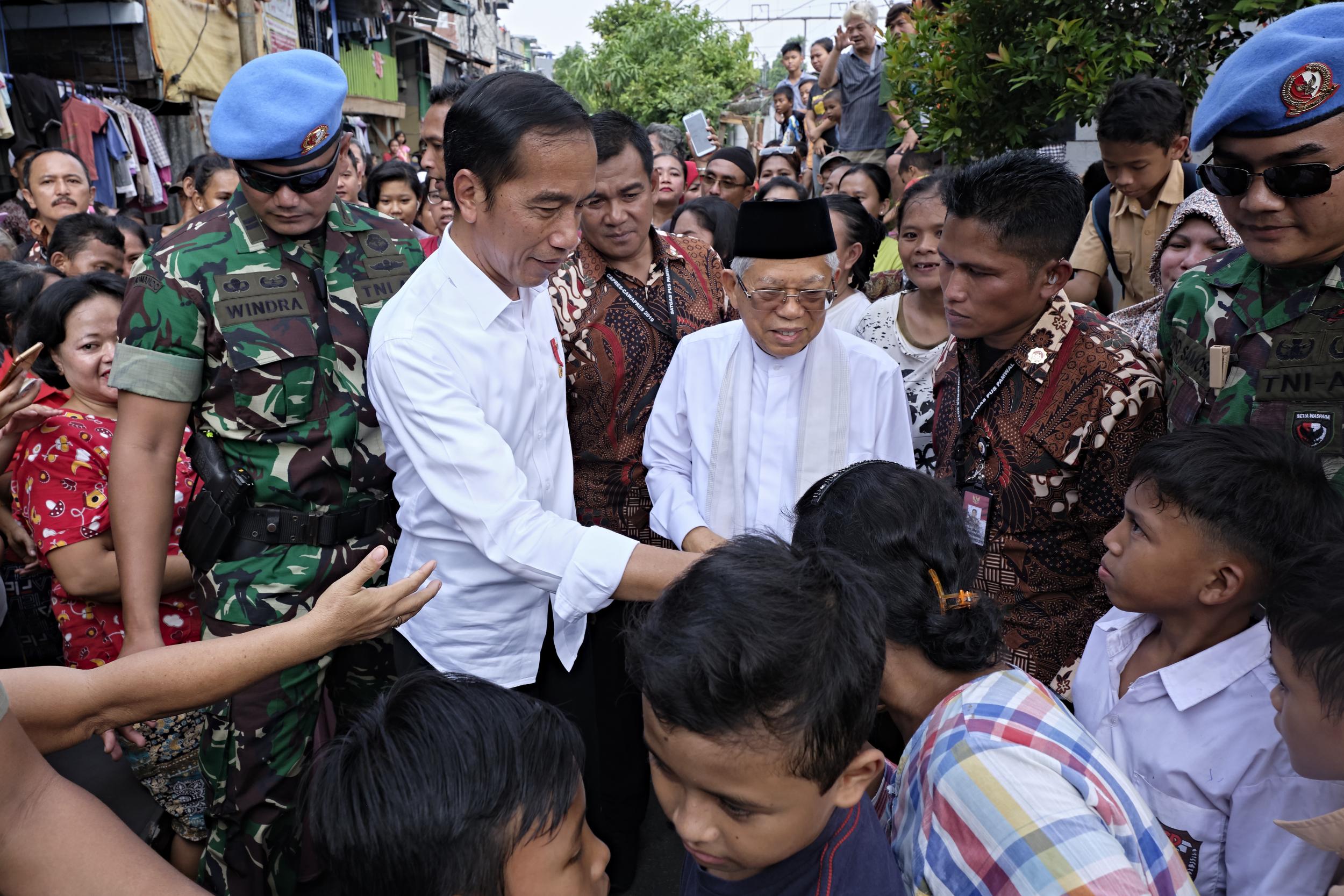 Indonesian president Joko Widodo, left, and his running mate Ma’ruf Amin shake hands while walking through a slum area in Jakarta