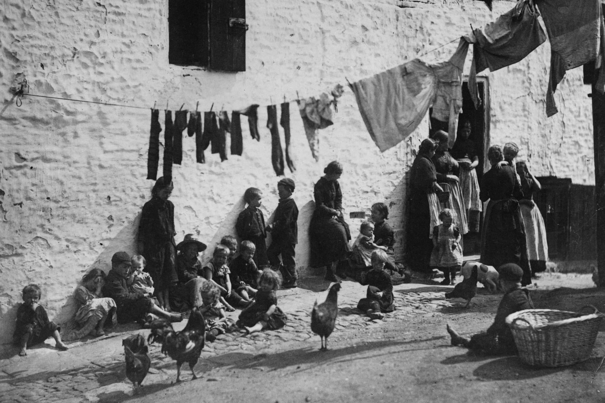 Children sit under a washing line hanging across a courtyard in a slum area of London in 1889 (Getty)