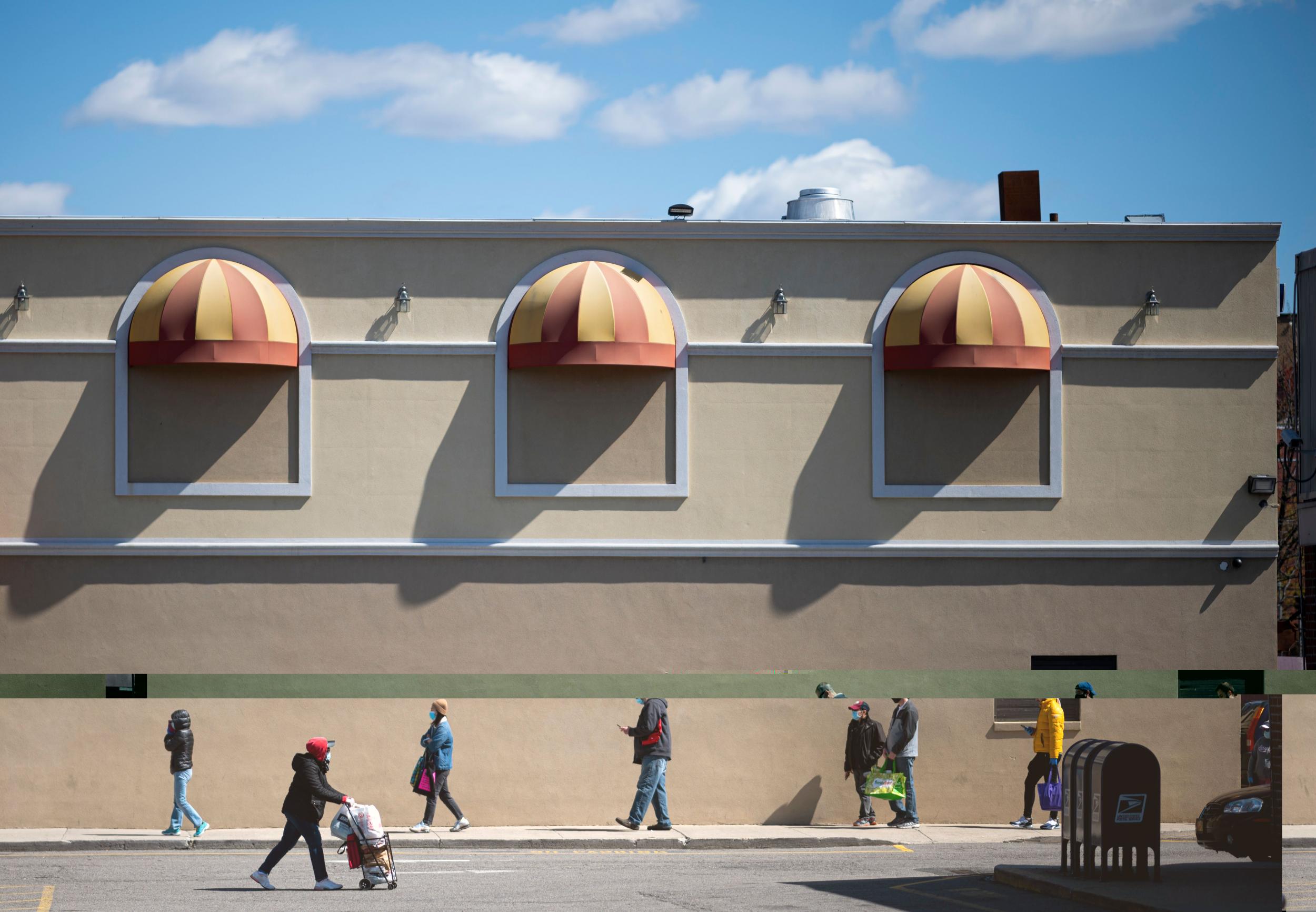 People keep social distance as they queue in front of the supermarket in New York