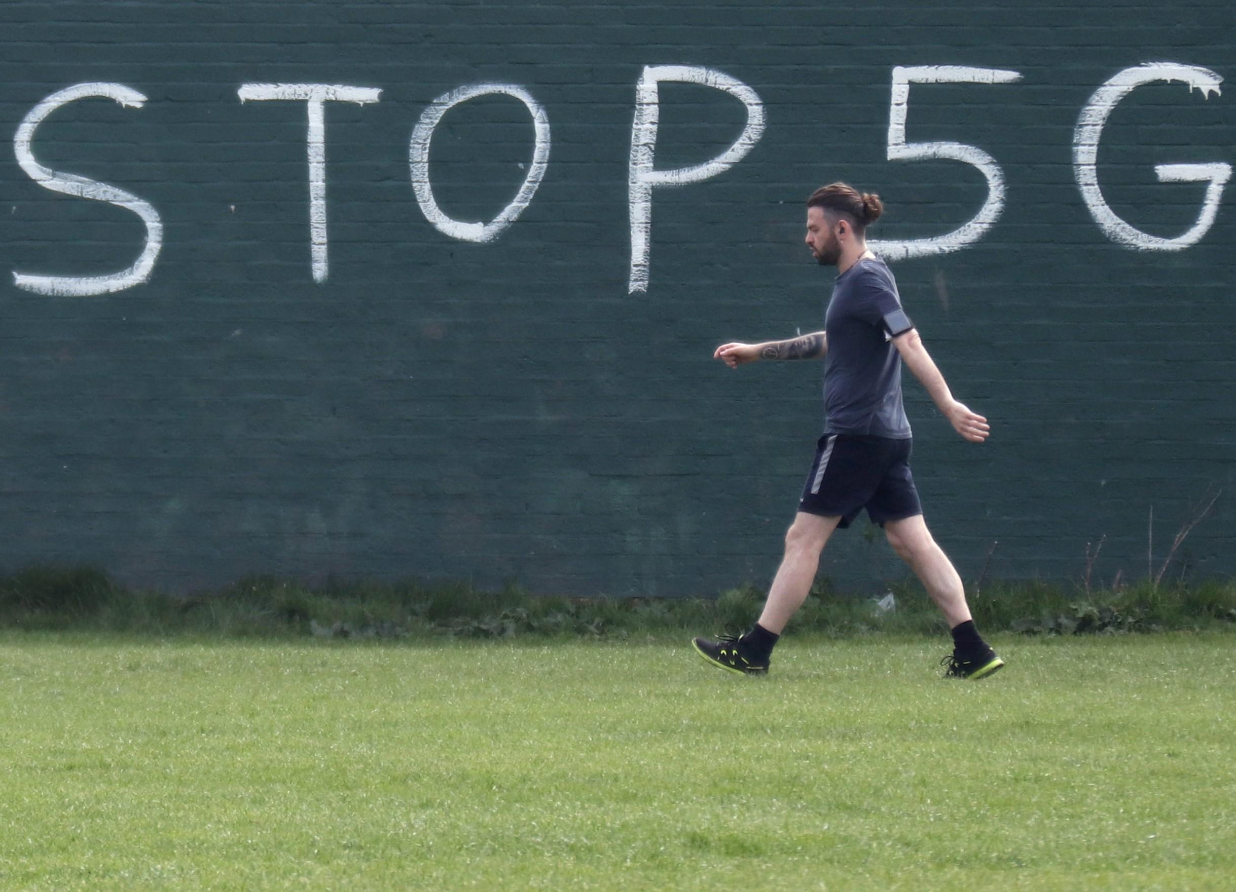 A man exercising during coronavirus lockdown walks past a graffiti that reads 'STOP 5G' in London, 8 April, 2020