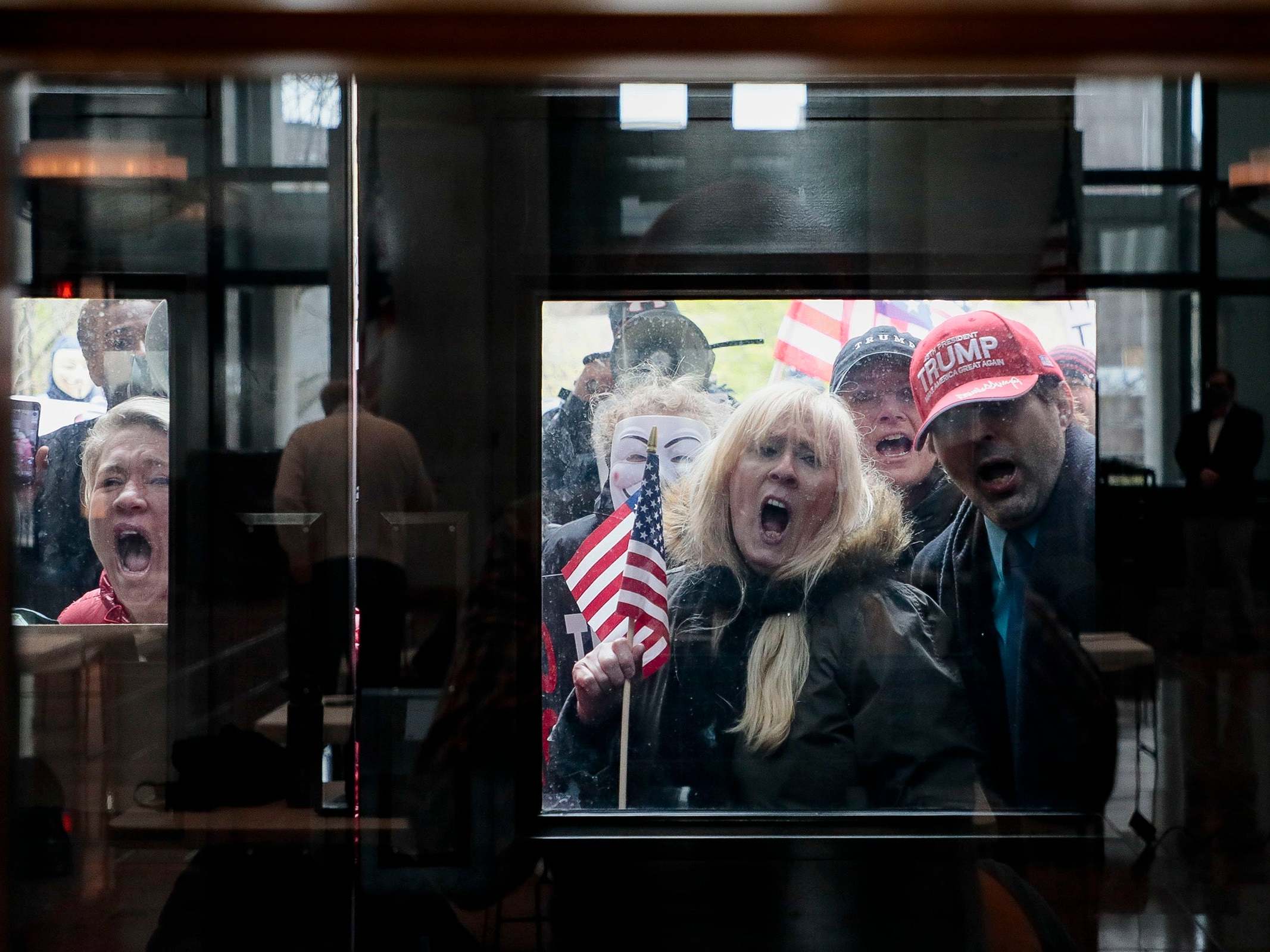 Protesters stand outside the Statehouse Atrium where reporters listen during the State of Ohio's Coronavirus response update on Monday, April 13, 2020 at the Ohio Statehouse in Columbus, Ohio. About 100 protesters assembled outside the building during Gov. Mike DeWine's weekday update on the state's response to the COVID-19 pandemic, upset that the state remains under a Stay-At-Home order and that non-essential businesses remain closed.