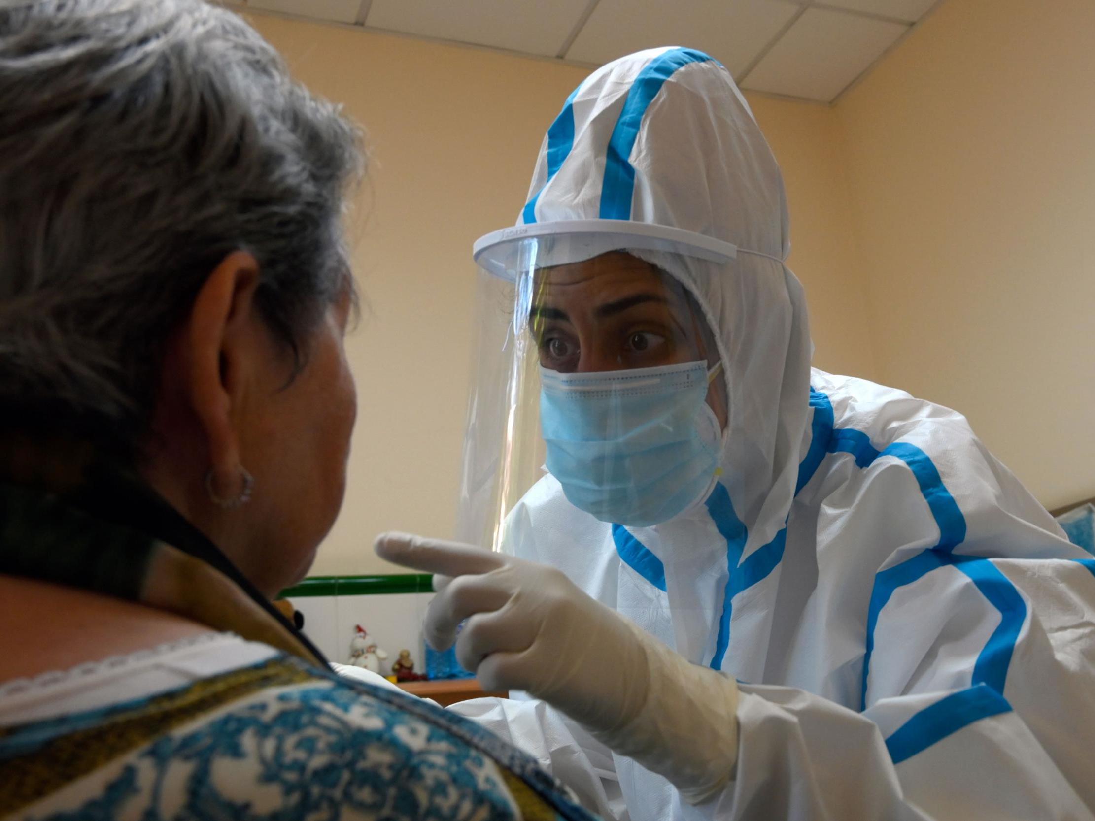 A healthcare worker wearing a protective suit takes a swab sample from a care home resident