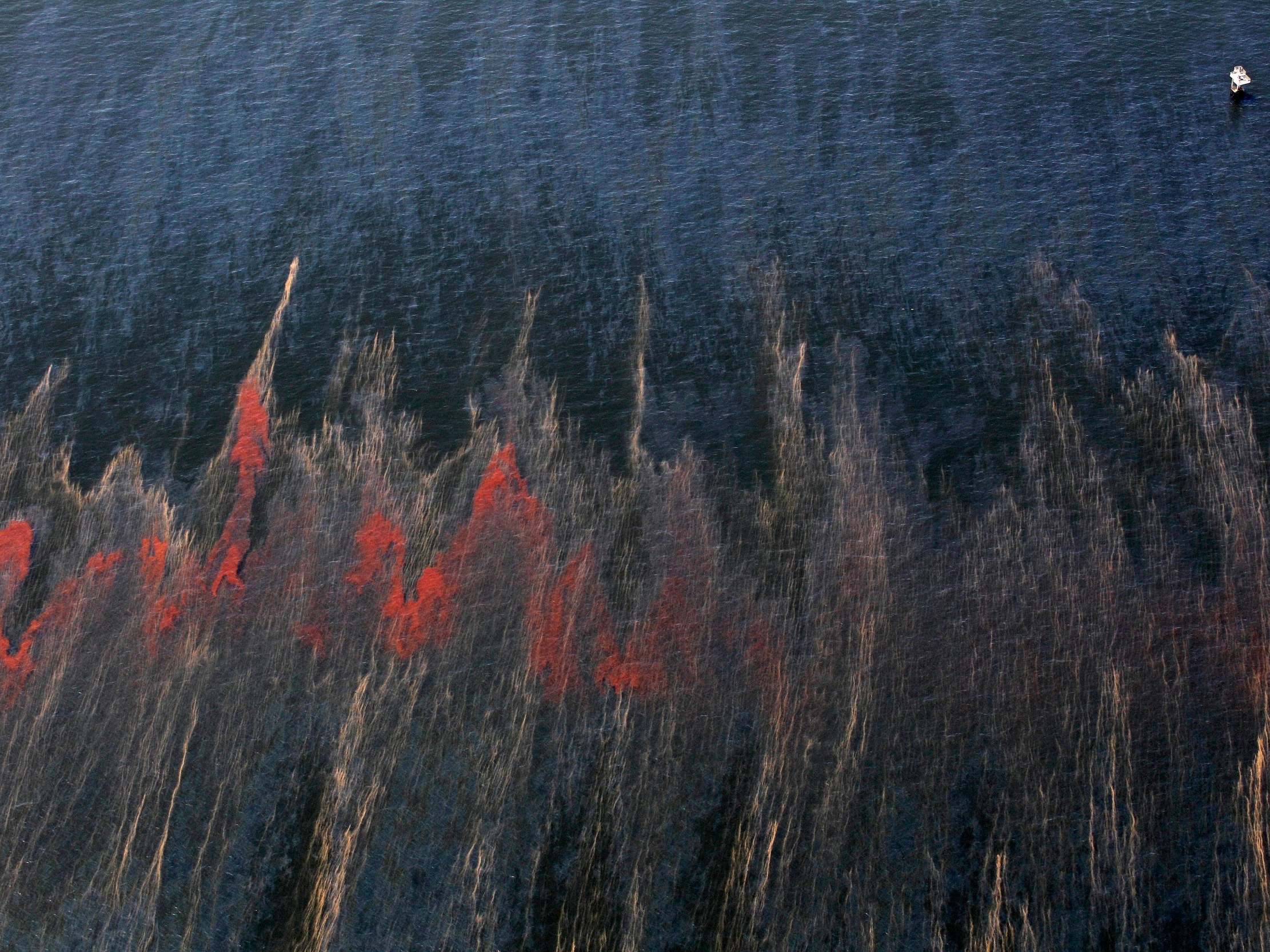 Oil is seen moving past an oil rig in the waters of Chandeleur Sound, Louisiana on May 5, 2010, weeks after the Deepwater Horizon explosion and oil spill (AP Photo/Eric Gay, File)