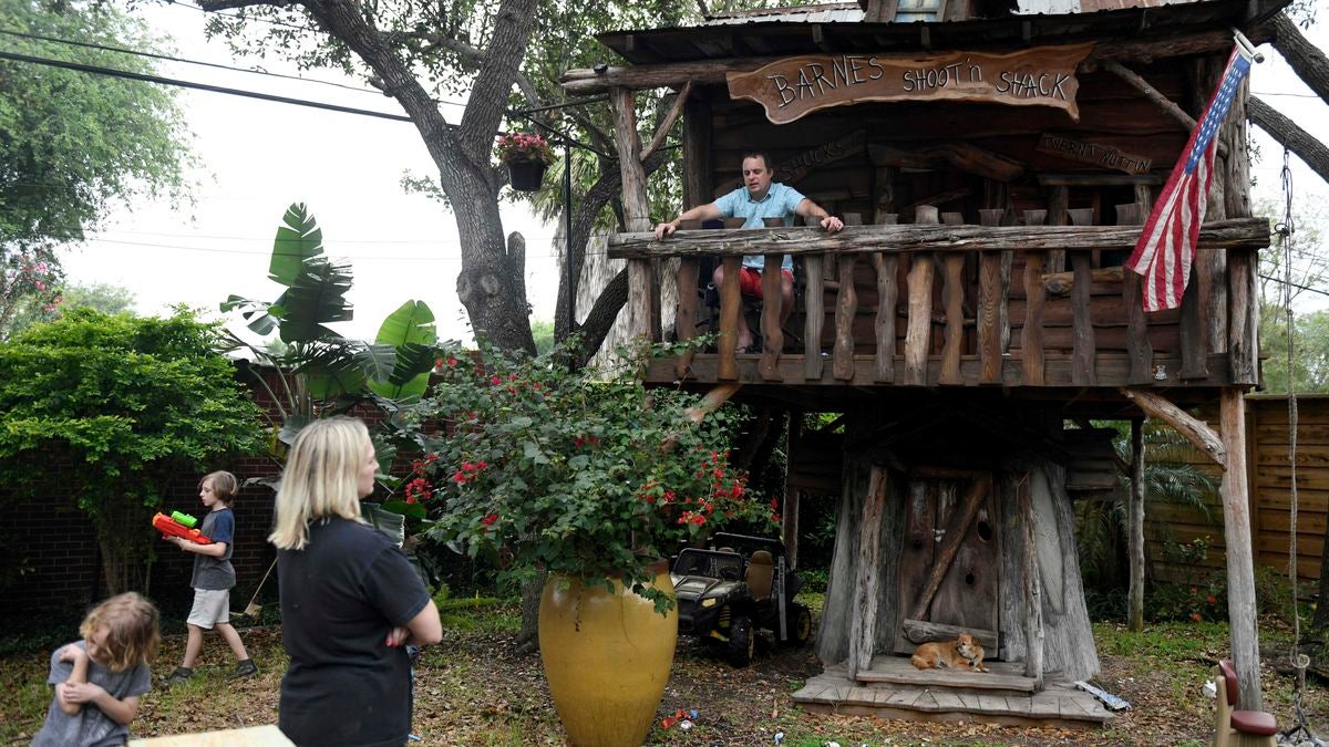 Barnes, top right, sits in his kids' treehouse while his family plays in their backyard in Corpus Christi, Texas