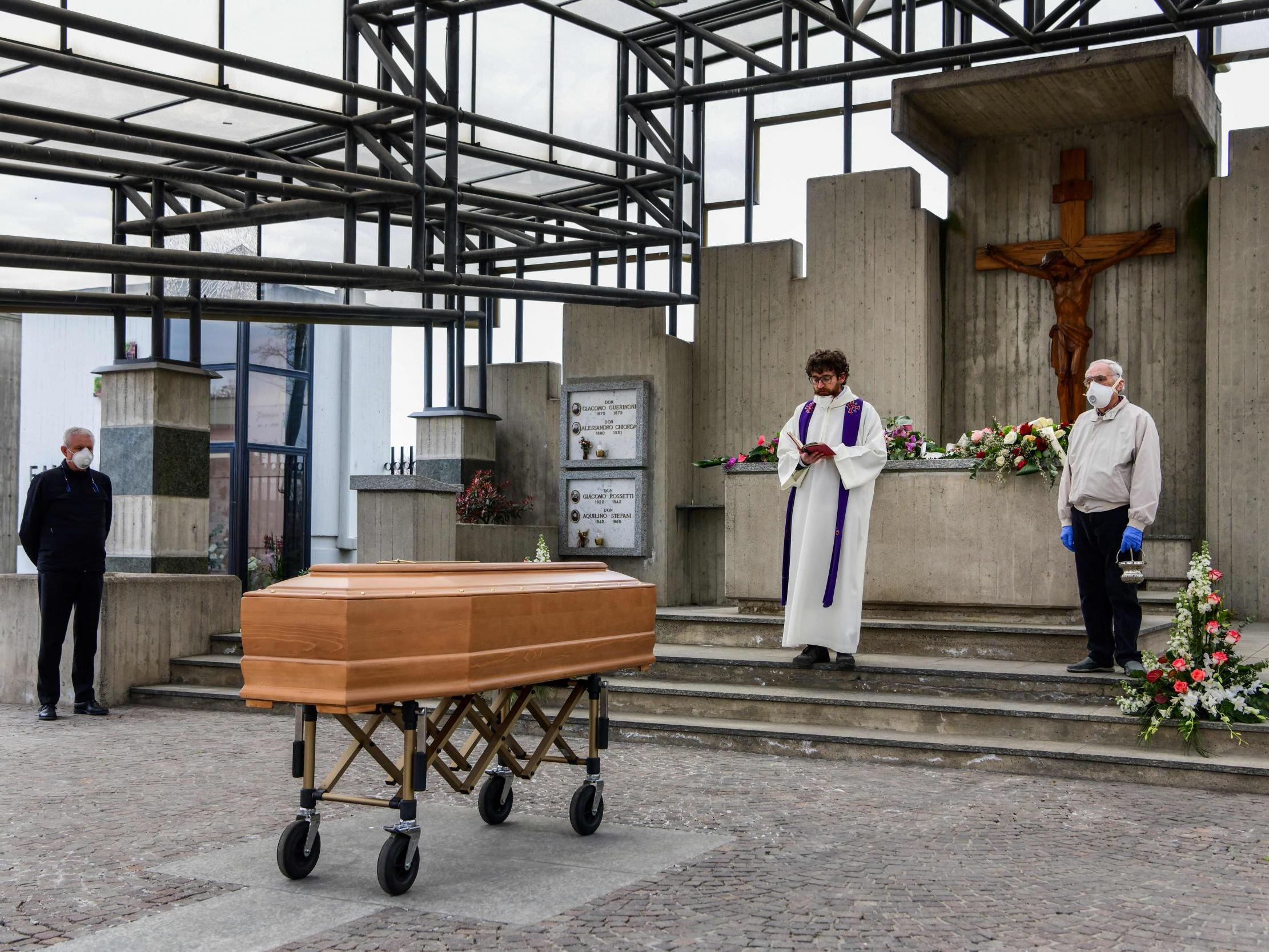 A priest reads prayers from the book of funeral rites in a northern Italian cemetery in the absence of relatives