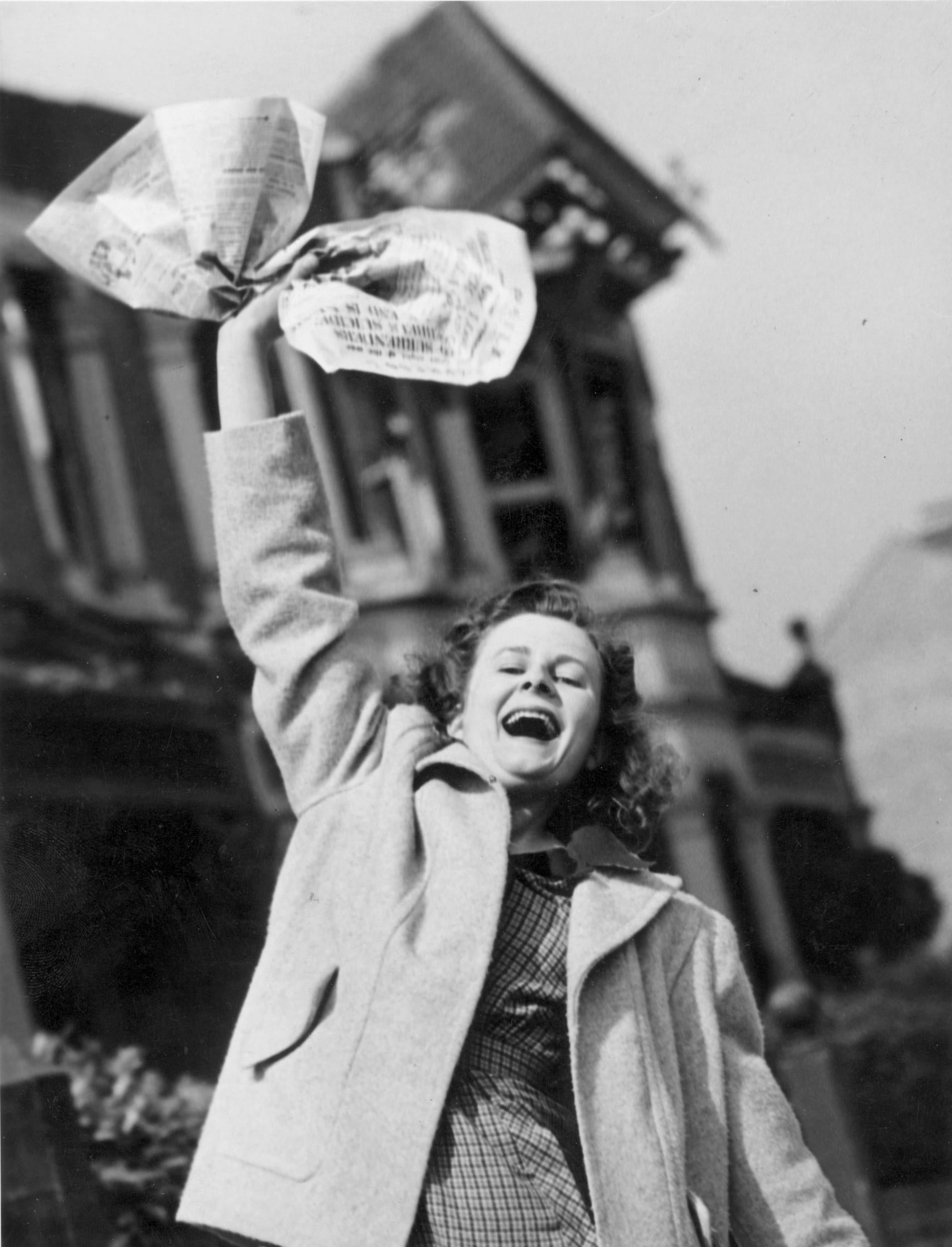 Mrs Pat Burgess of Palmers Green, North London waves a newspaper containing the news of Germany’s surrender in World War II