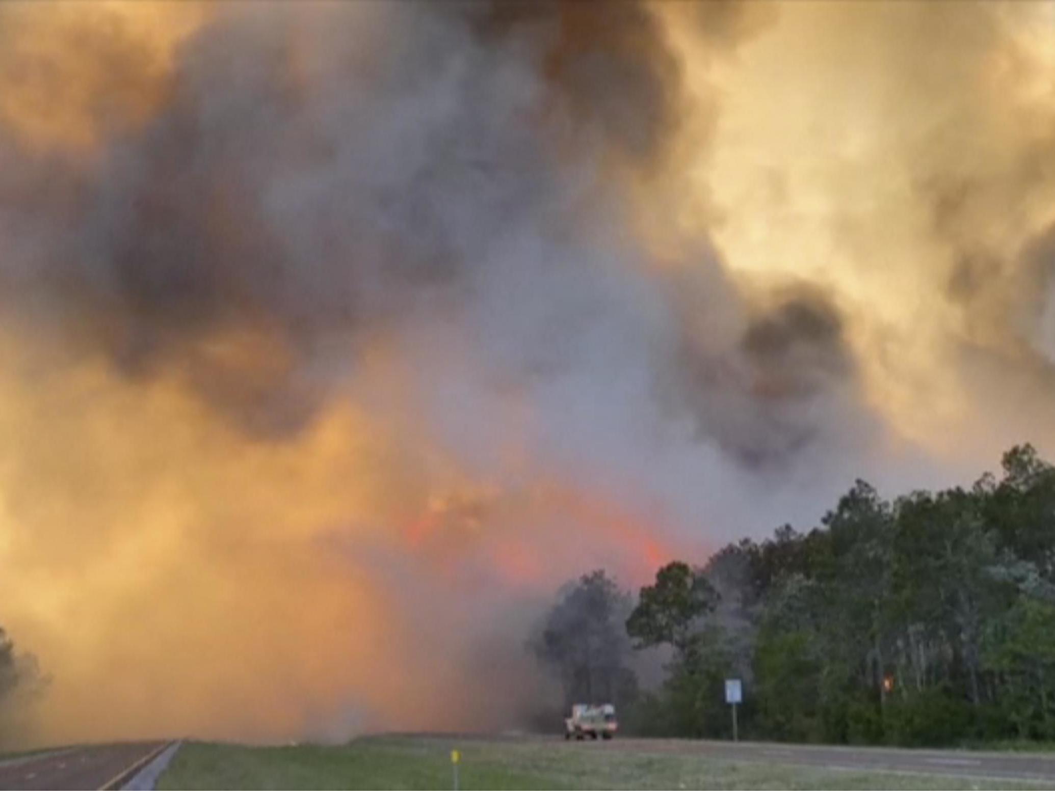 Fire and smoke rise from trees alongside a road in Santa Rosa County
