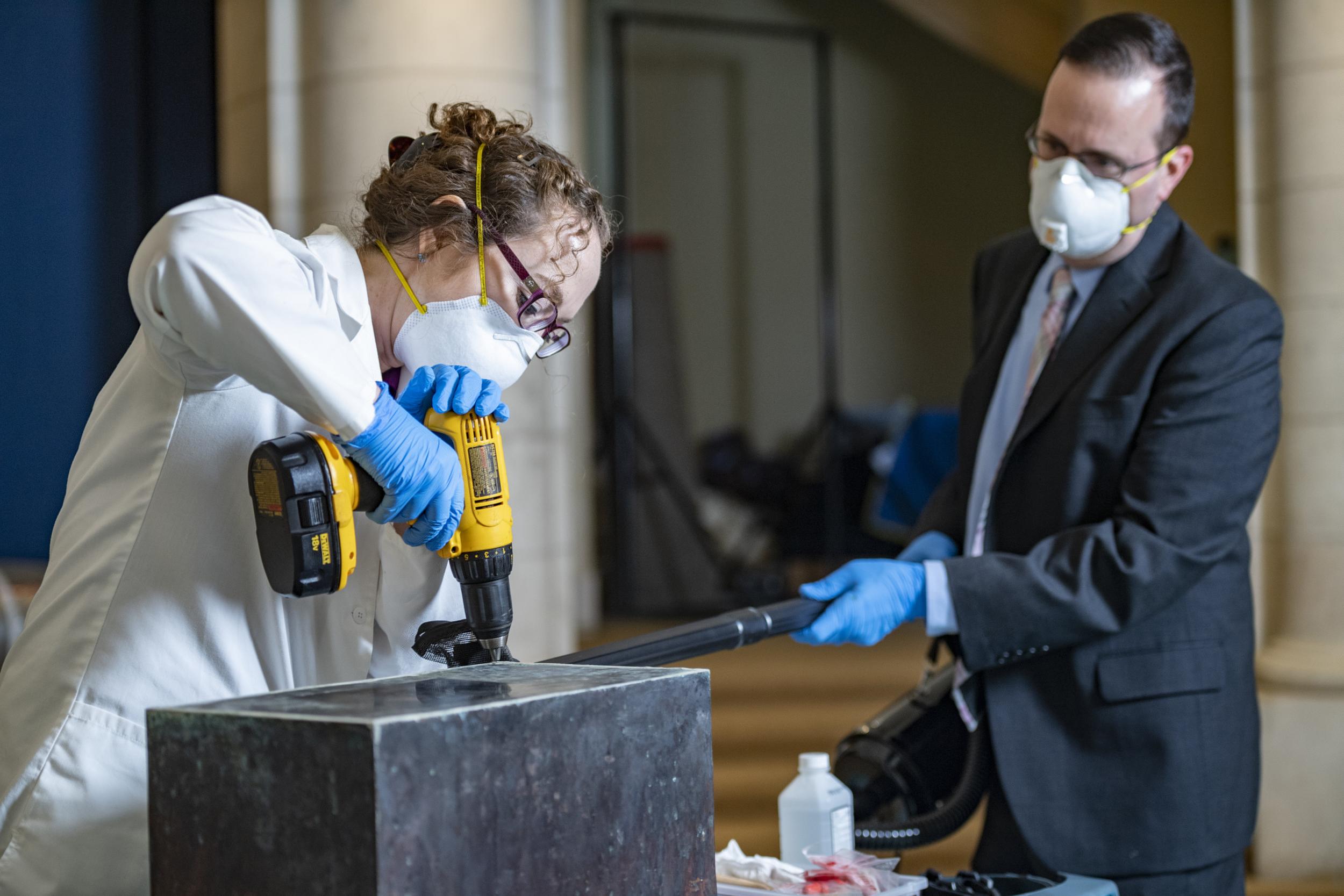 Conservator Caitlin Smith (left) and historian Tim Frank work last month to open the time capsule placed in the cornerstone of Memorial Amphitheater at Arlington National Cemetery in 1915