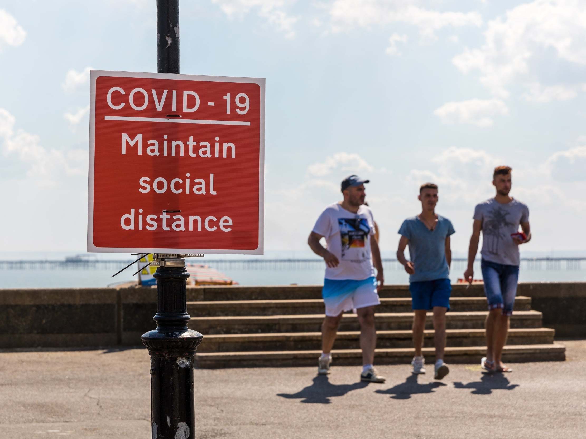 Visitors to Southend beach walk past a social distancing warning sign