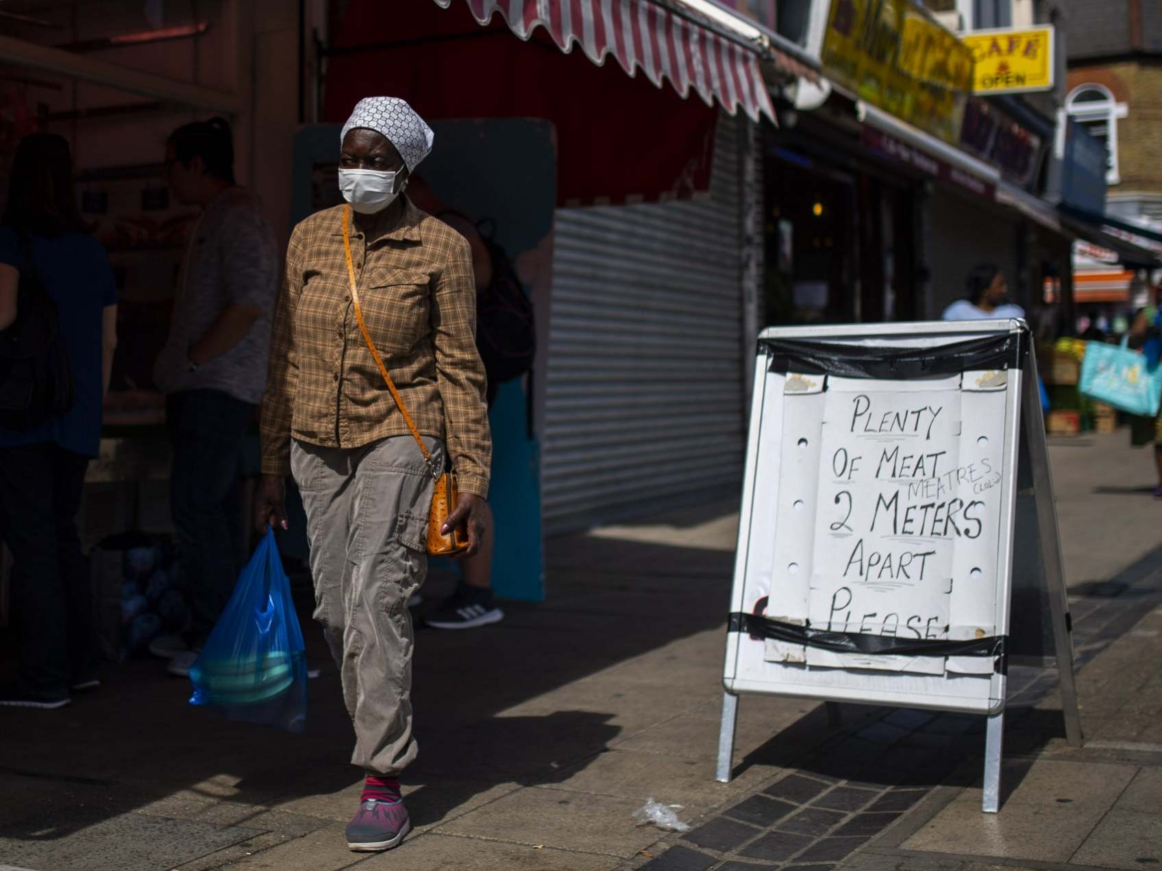 A woman walks past a social distancing sign outside a butchers in Walthamstow, London