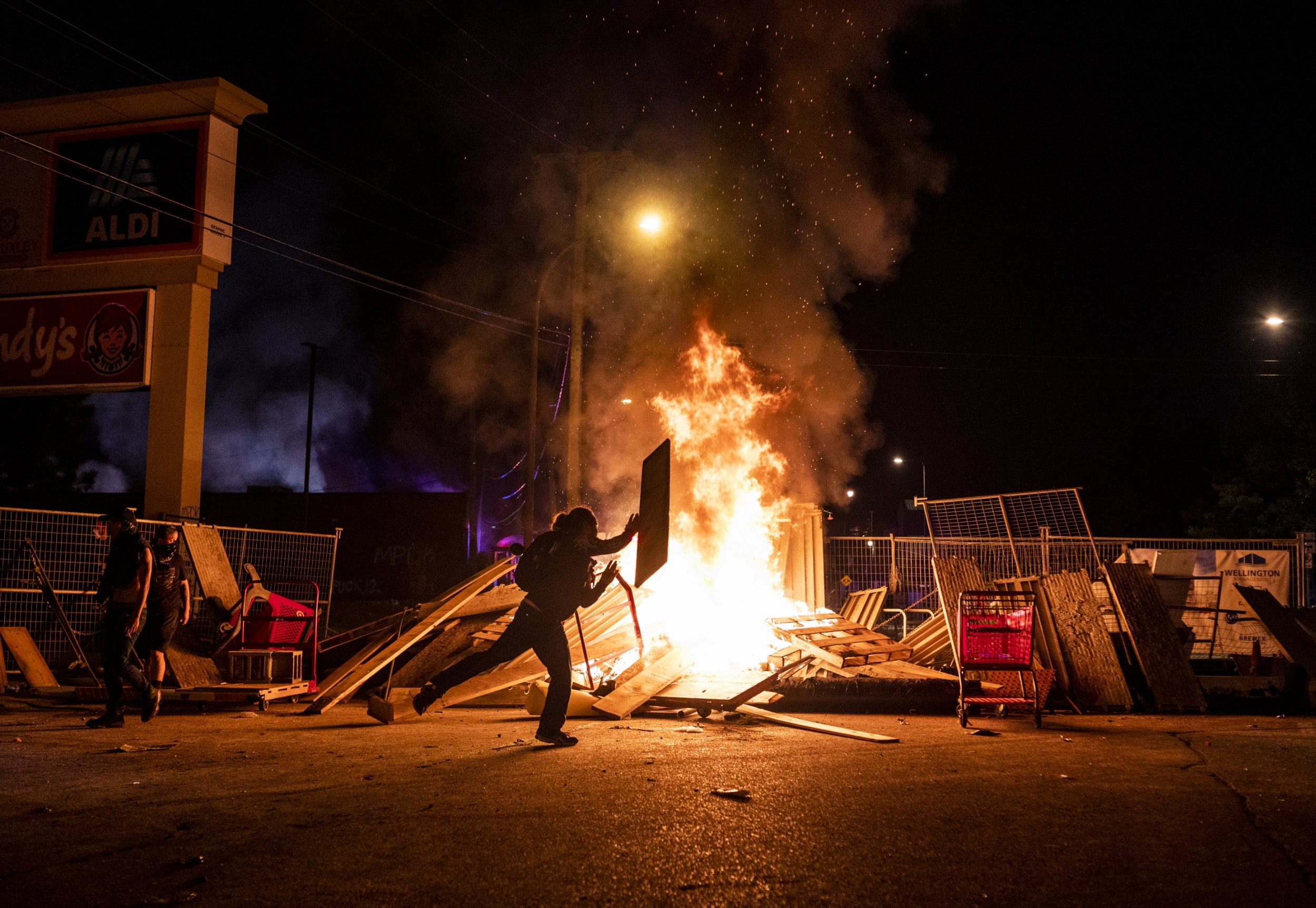 A protester throws a piece of wood on a fire in the street just north of the 3rd Police Precinct