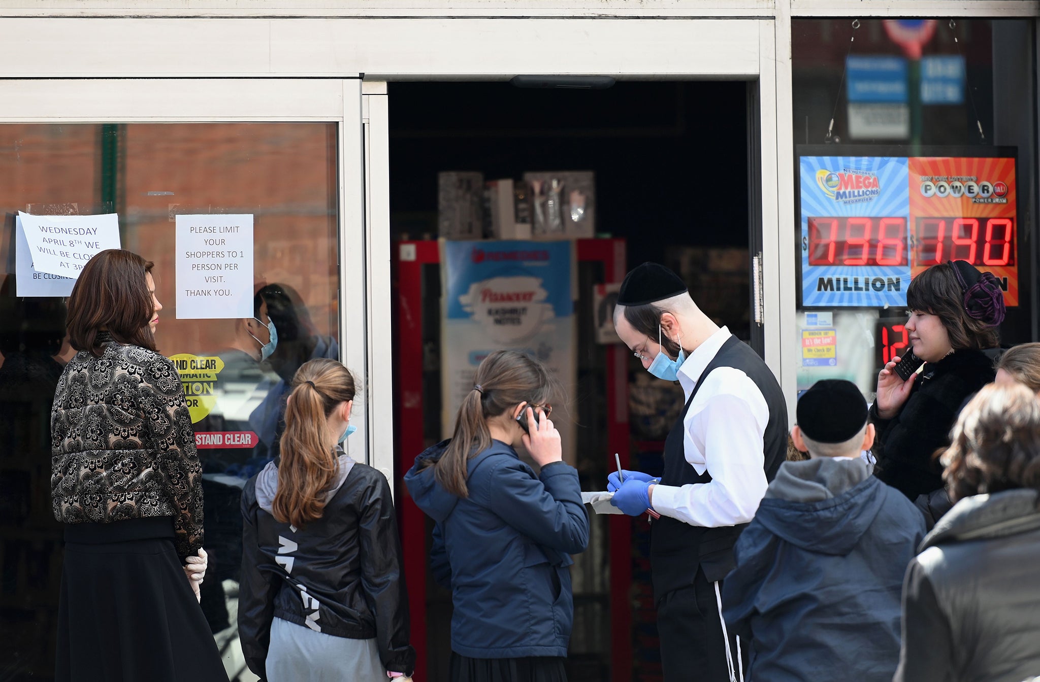 Members of the Orthodox Jewish community queue to enter a pharmacy at the start of the family-orientated Passover holiday