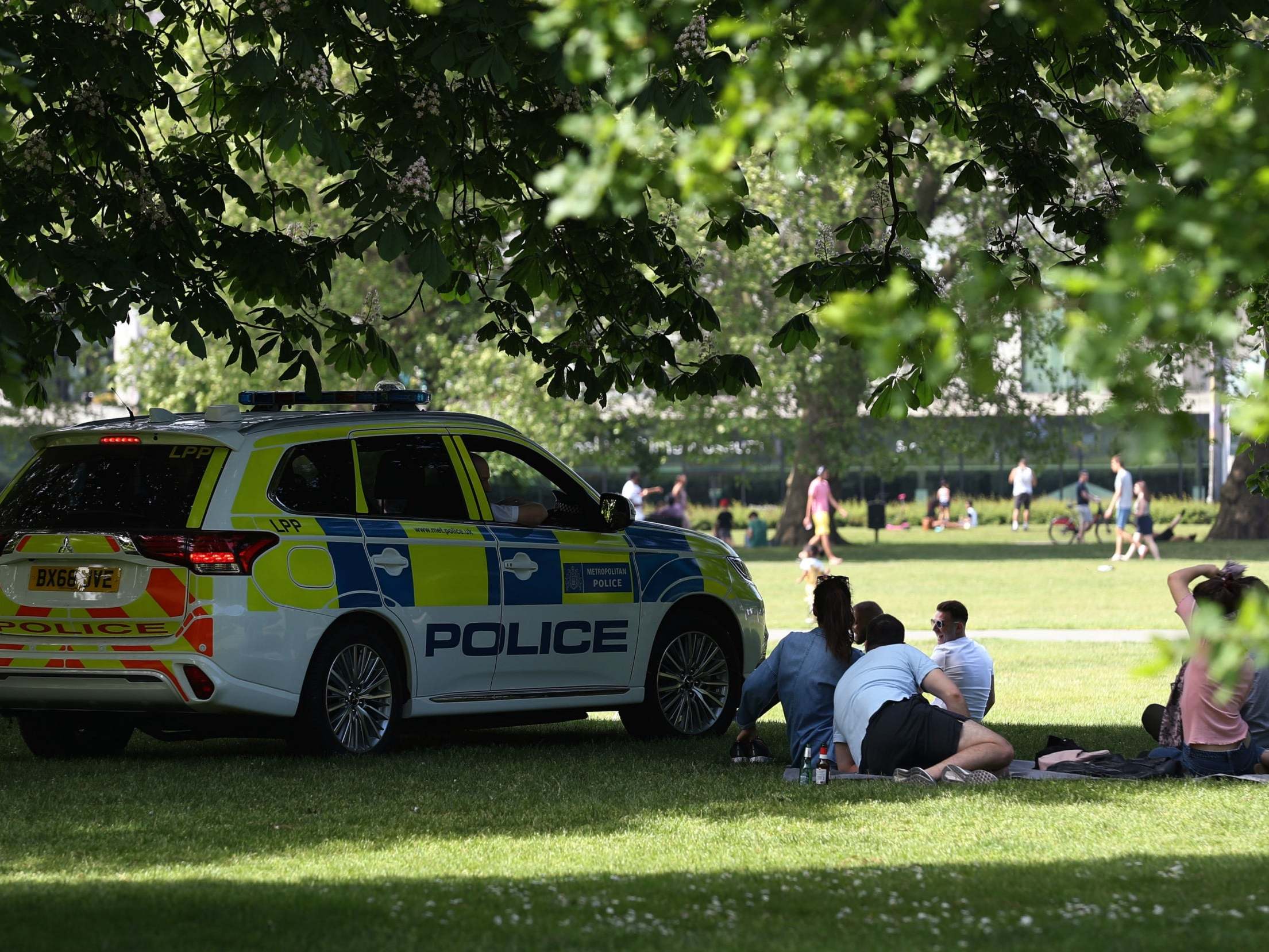 Police officers in a patrol car move sunbathers on in Greenwich Park