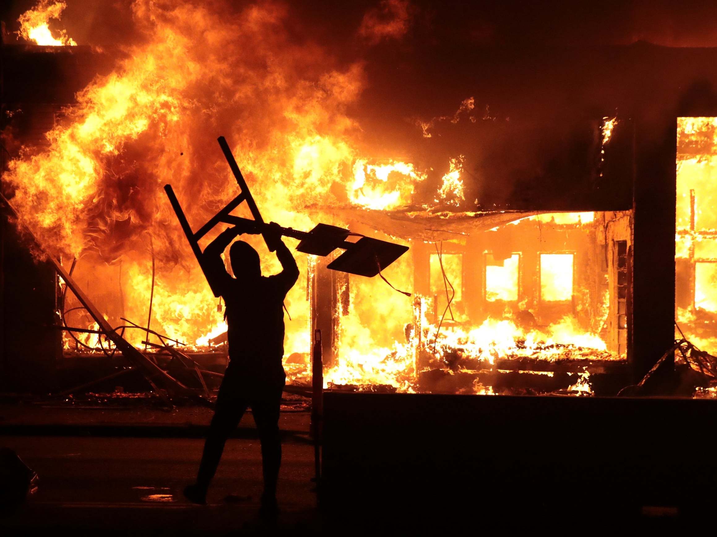 A man holds up a sign near a burning building during protests sparked by the death of George Floyd while in police custody