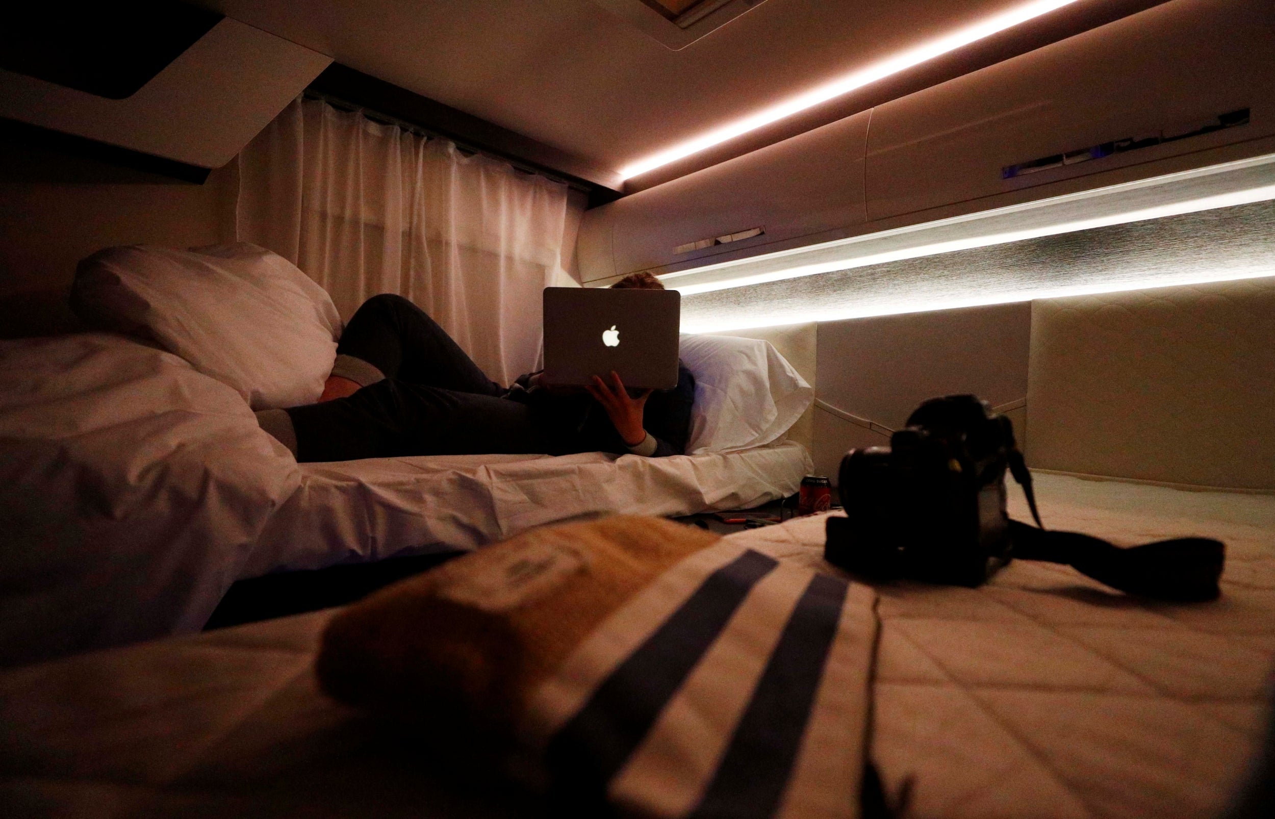 Hannah edits images on her laptop, as she lies on a bed in a motorhome