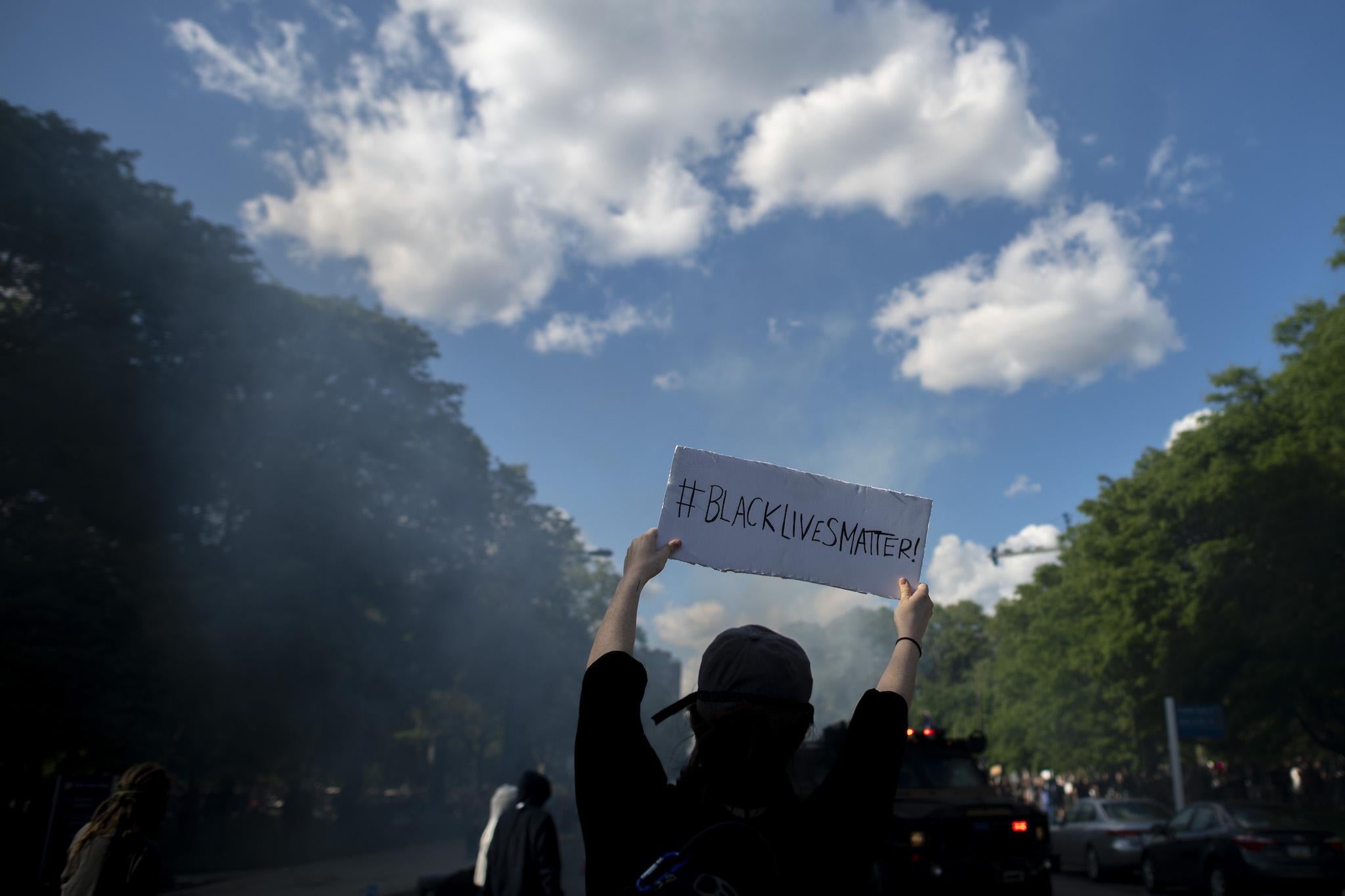 A protester holds a sign stating "BLACK LIVES MATTER" towards police shooting tear gas after a march through Center City on June 1, 2020 in Philadelphia, Pennsylvania