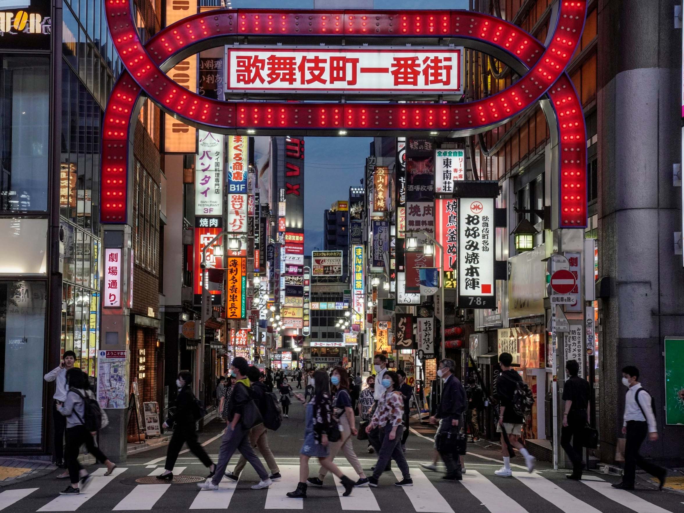 Commuters walk toward a railway station in front of an entrance to Kabukicho, Japan's biggest nightlife entertainment district at Shinjuku, in Tokyo, 25 May 2020.