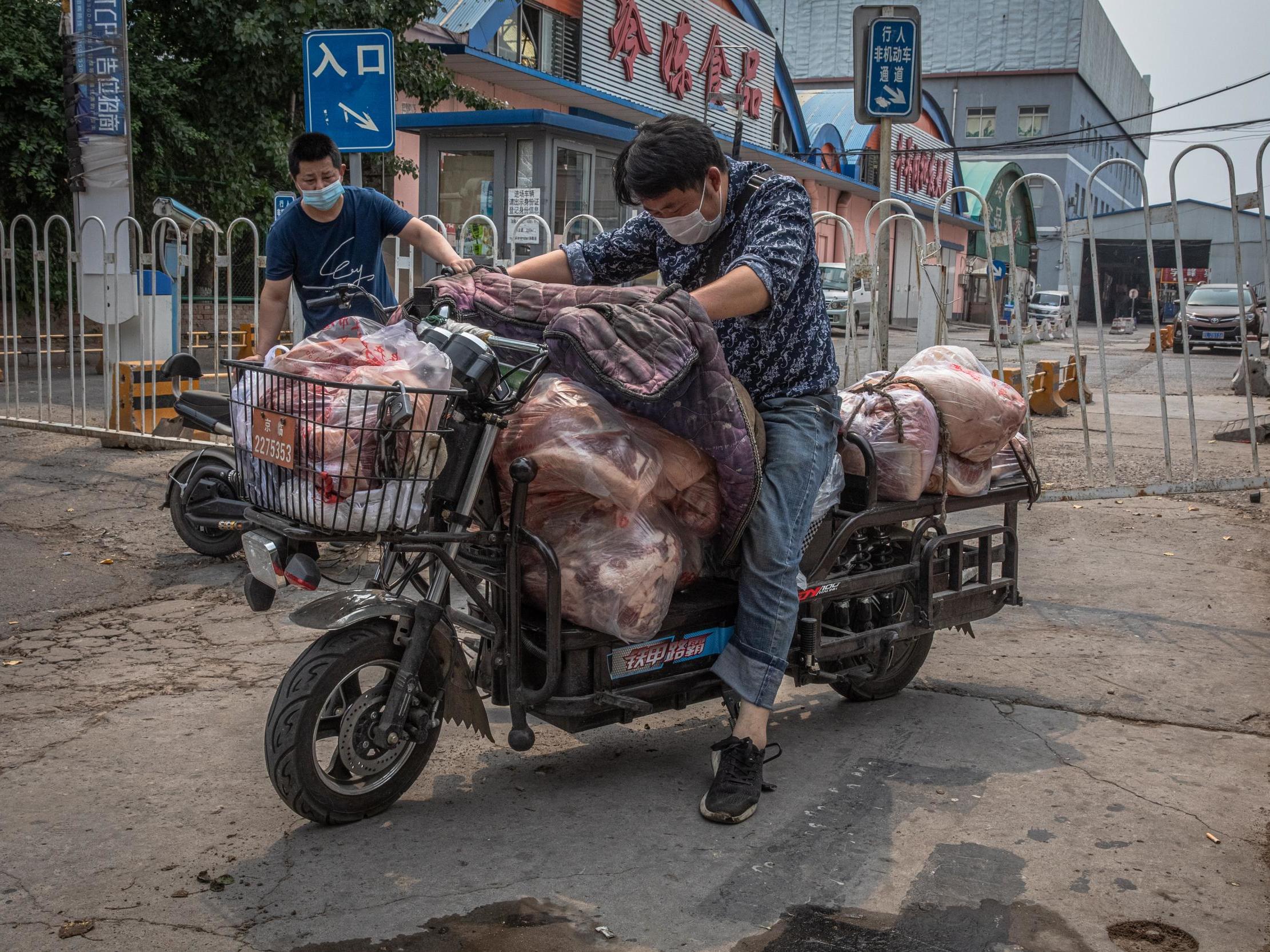 Men in face masks load a scooter with meat after the Beijing market was closed