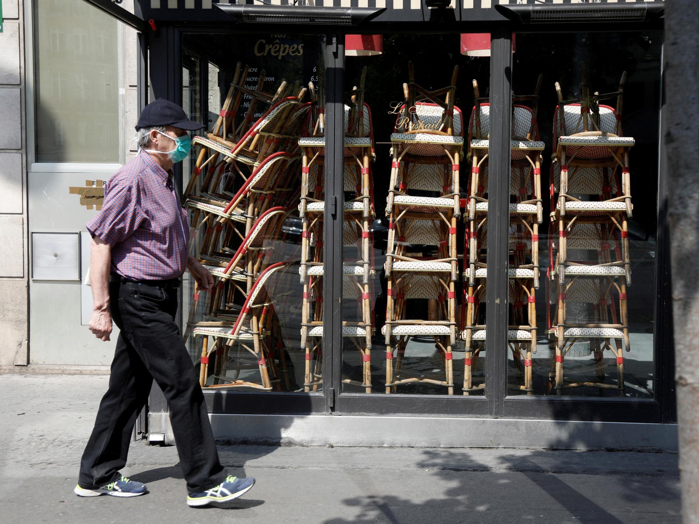 A man, wearing a protective face mask, passes by a closed cafe in Paris.