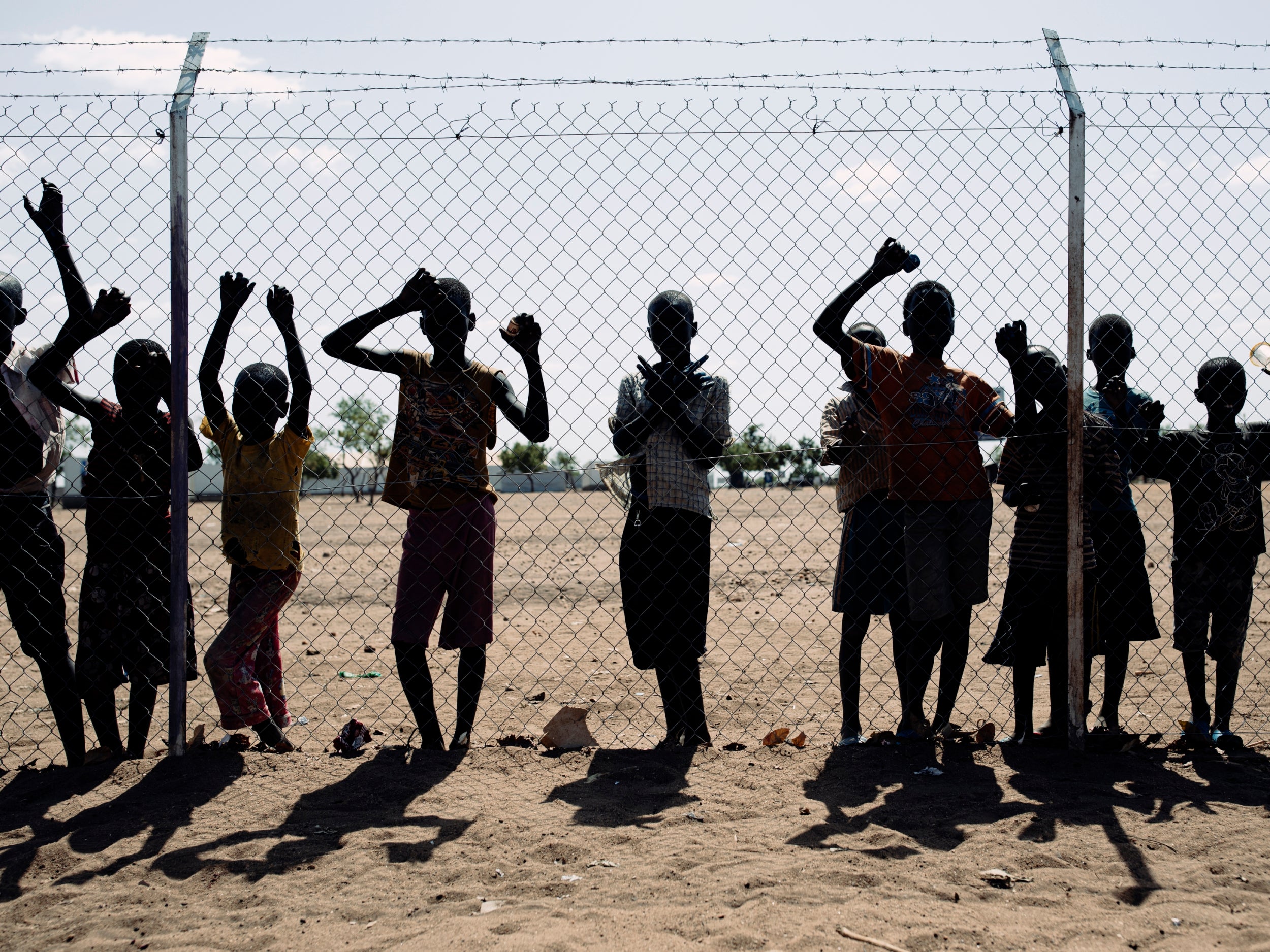 Children stand outside the perimeter fence of a school in Bidibidi refugee settlement