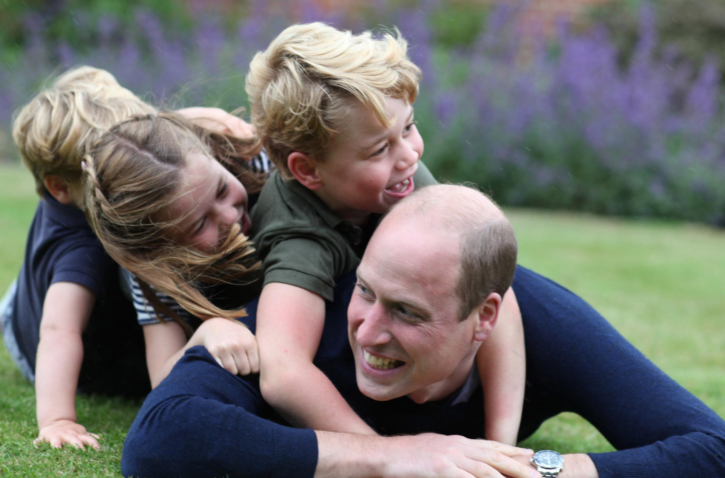 New photo shows Prince George, Princess Charlotte and Prince Louis clamber on top of their father as he lies smiling on the ground (Getty)