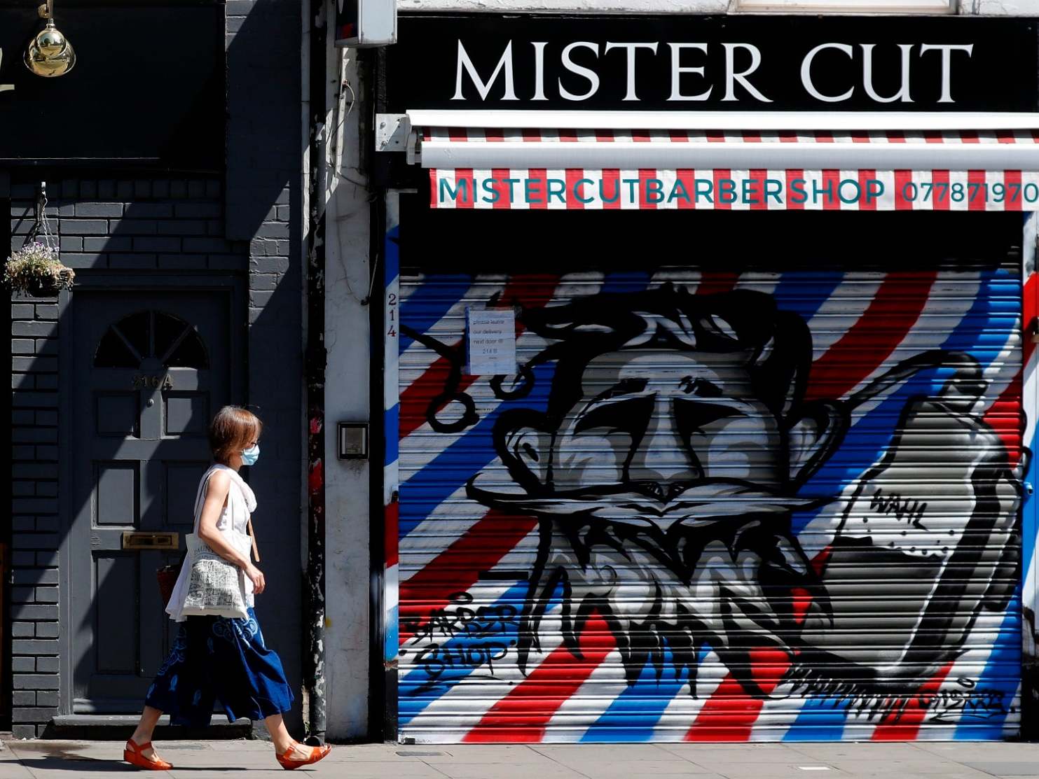 A woman walks by a closed barber shop in London