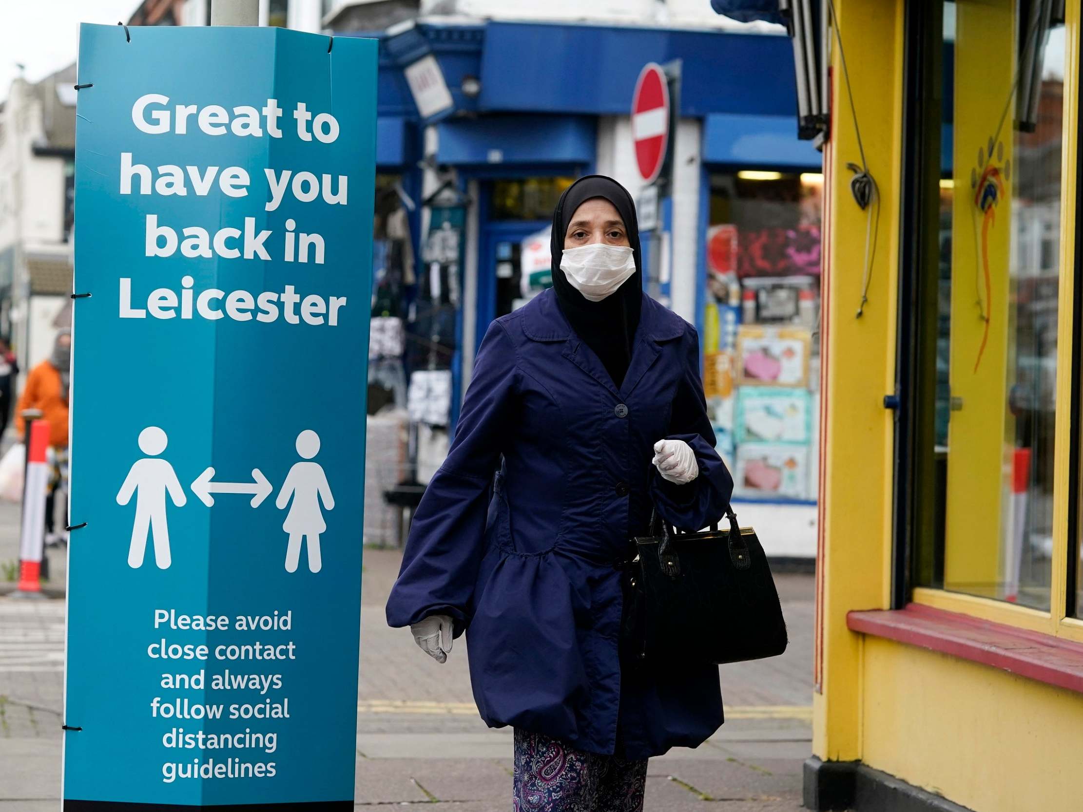 A woman wearing a PPE mask walks past social distance advisory signs in Leicester's North Evington neighbourhood on June 29, 2020 in Leicester, England.