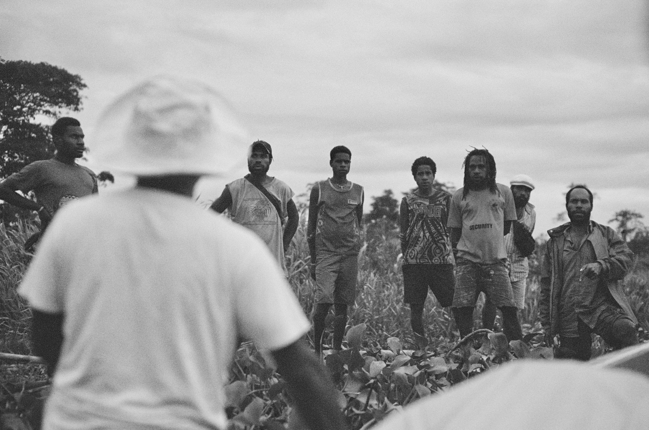 Manu descends from the canoe to inform villagers about a meeting in the Spirit House