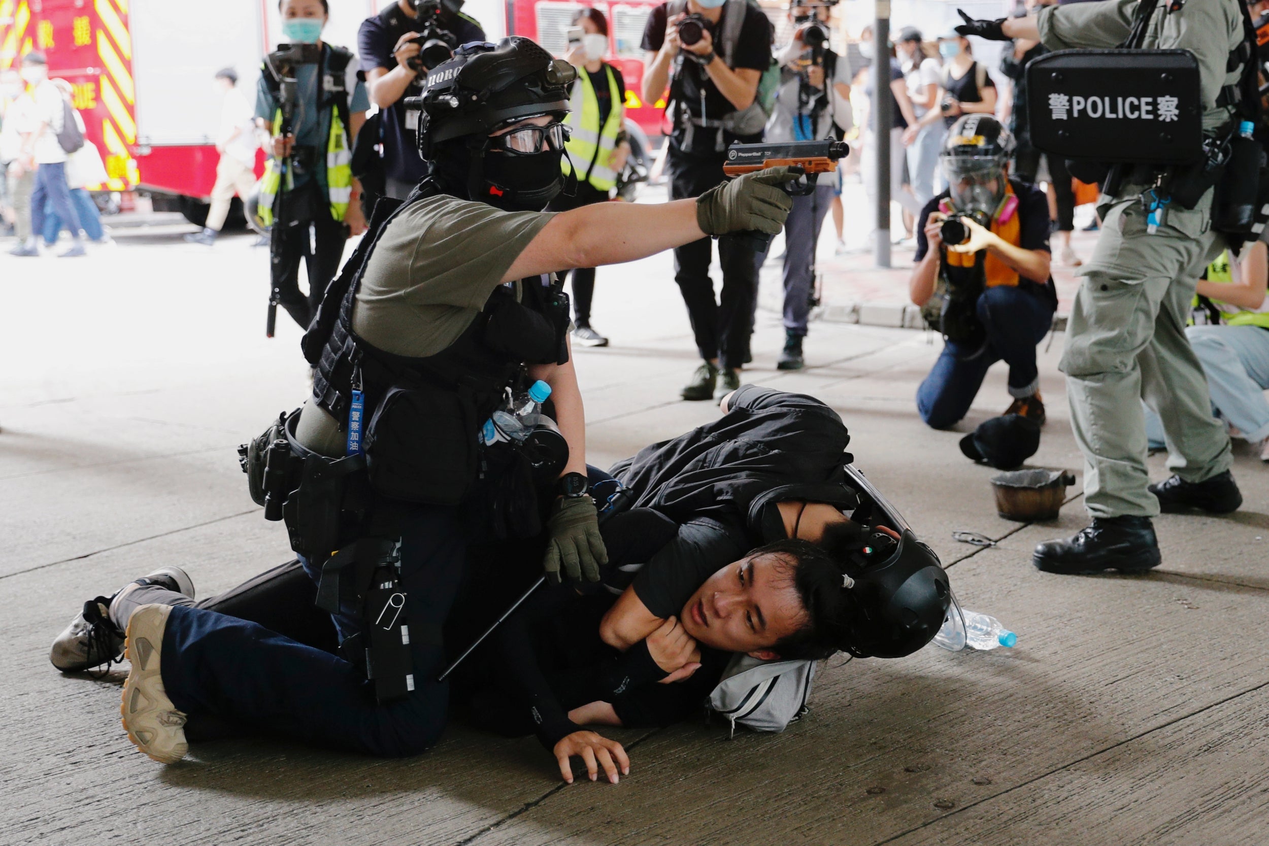 A Hong Kong police officer raises his pepper spray handgun as a man is detained during a march against the national security law