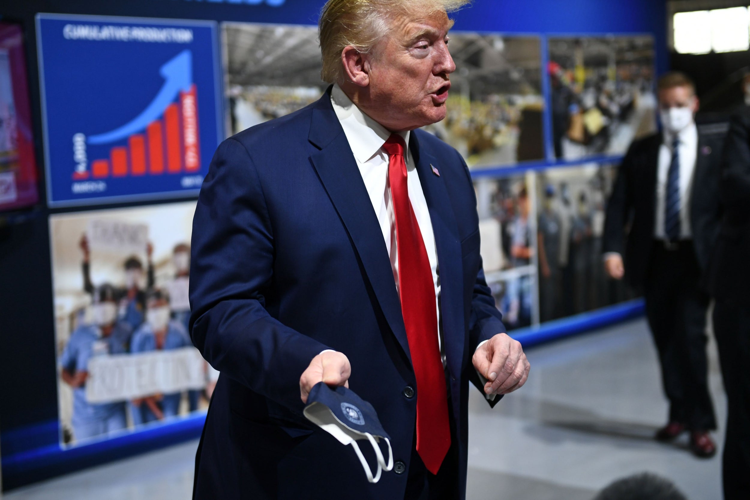 Donald Trump holds a face mask emblazoned with the presidential seal on a visit to a Ford manufacturing plant in Michigan