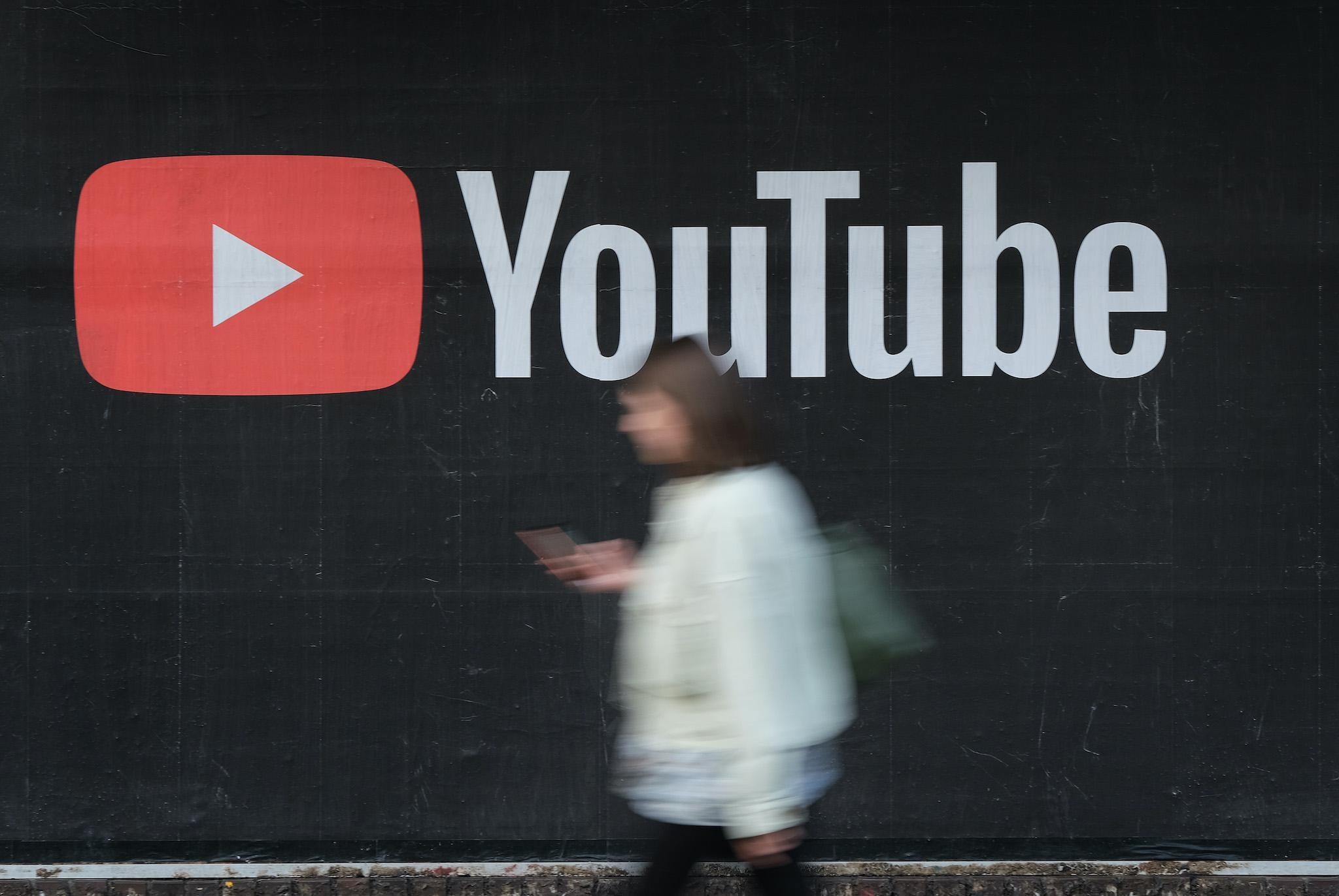 A young woman with a smartphone walks past a billboard advertisement for YouTube on September 27, 2019 in Berlin, Germany