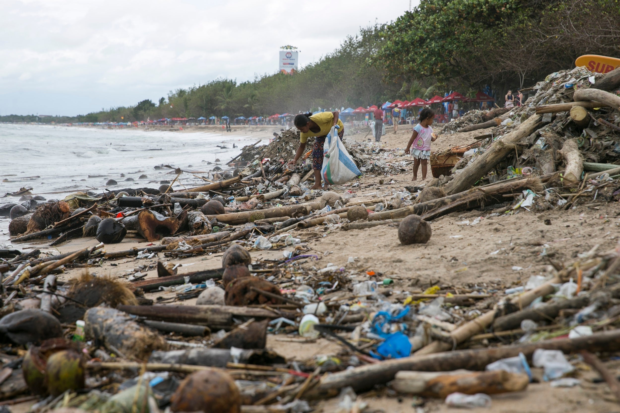 Scavengers collect recyclable materials from debris brought in by strong waves on a beach in Kuta, Bali
