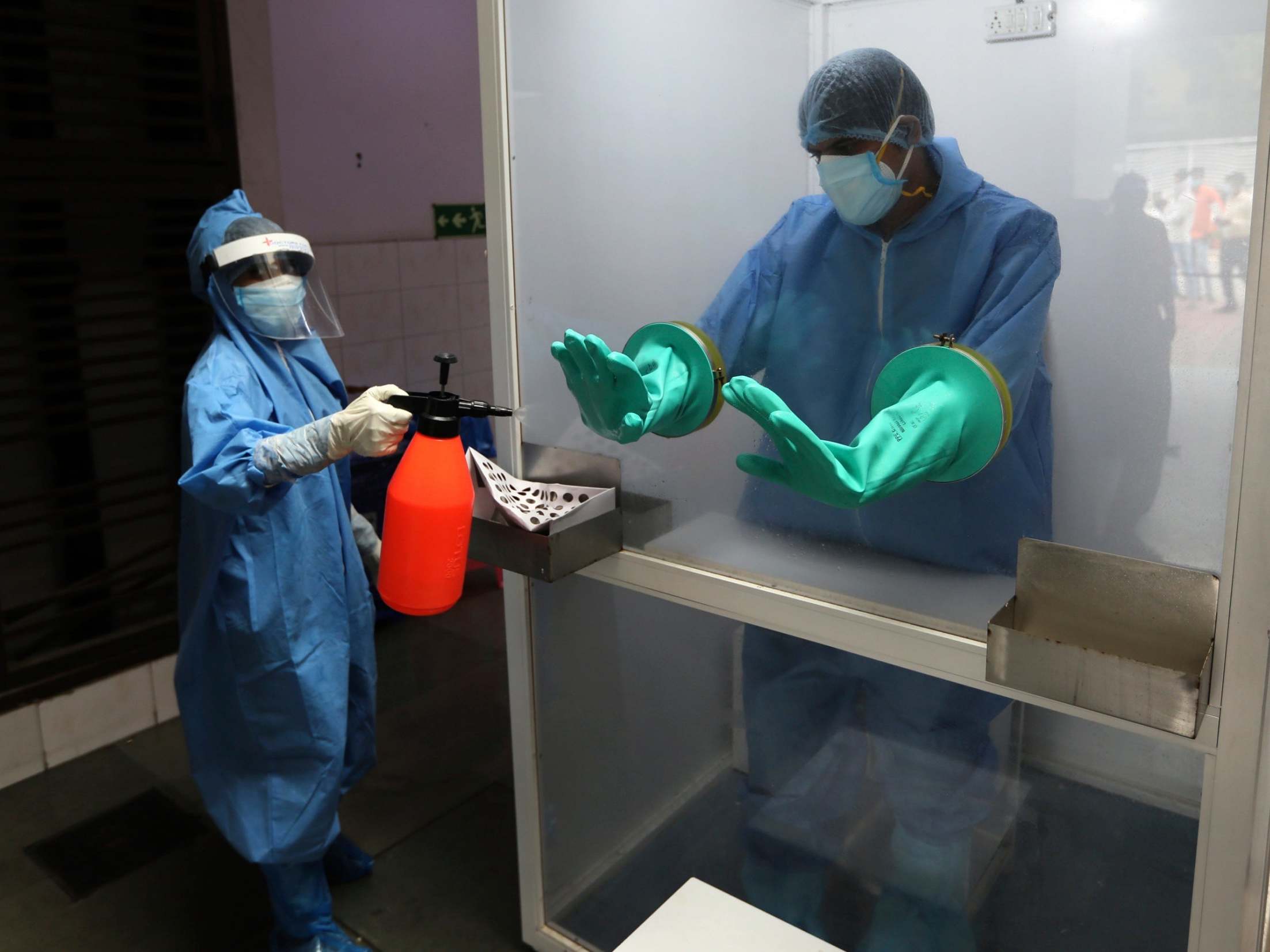 A health worker sanitises the gloves of another member of staff inside a booth in New Delhi