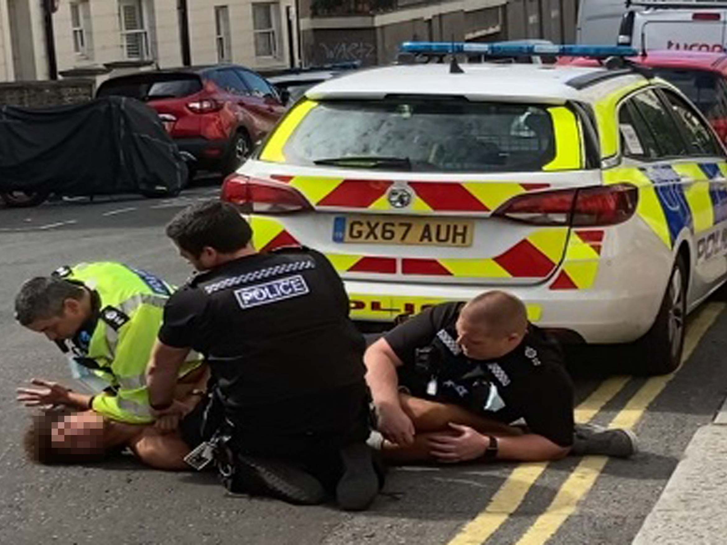 A man lies on the ground as he is restrained by three Sussex Police officers during an arrest in Brighton on 7 July 2020.