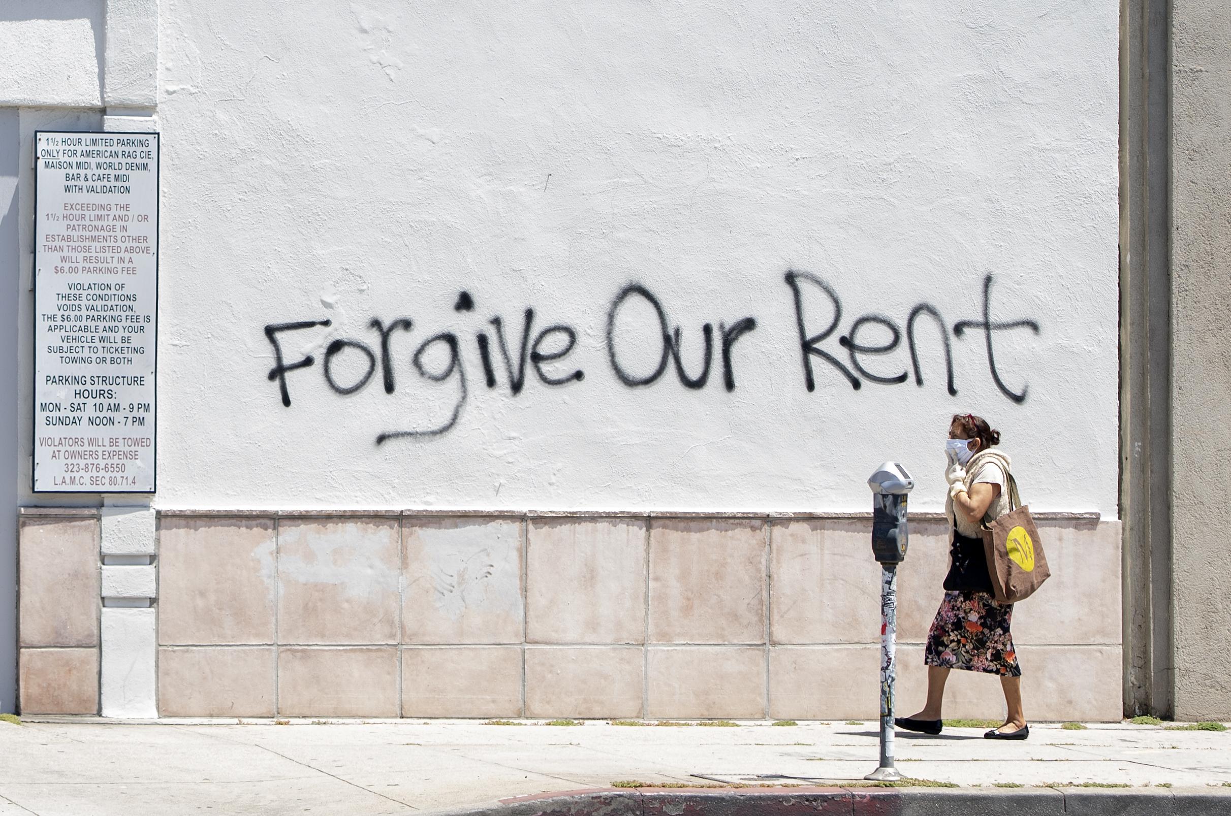 A woman walks past a wall bearing a graffiti asking for rent forgiveness on 1 May 2020 in Los Angeles, California.