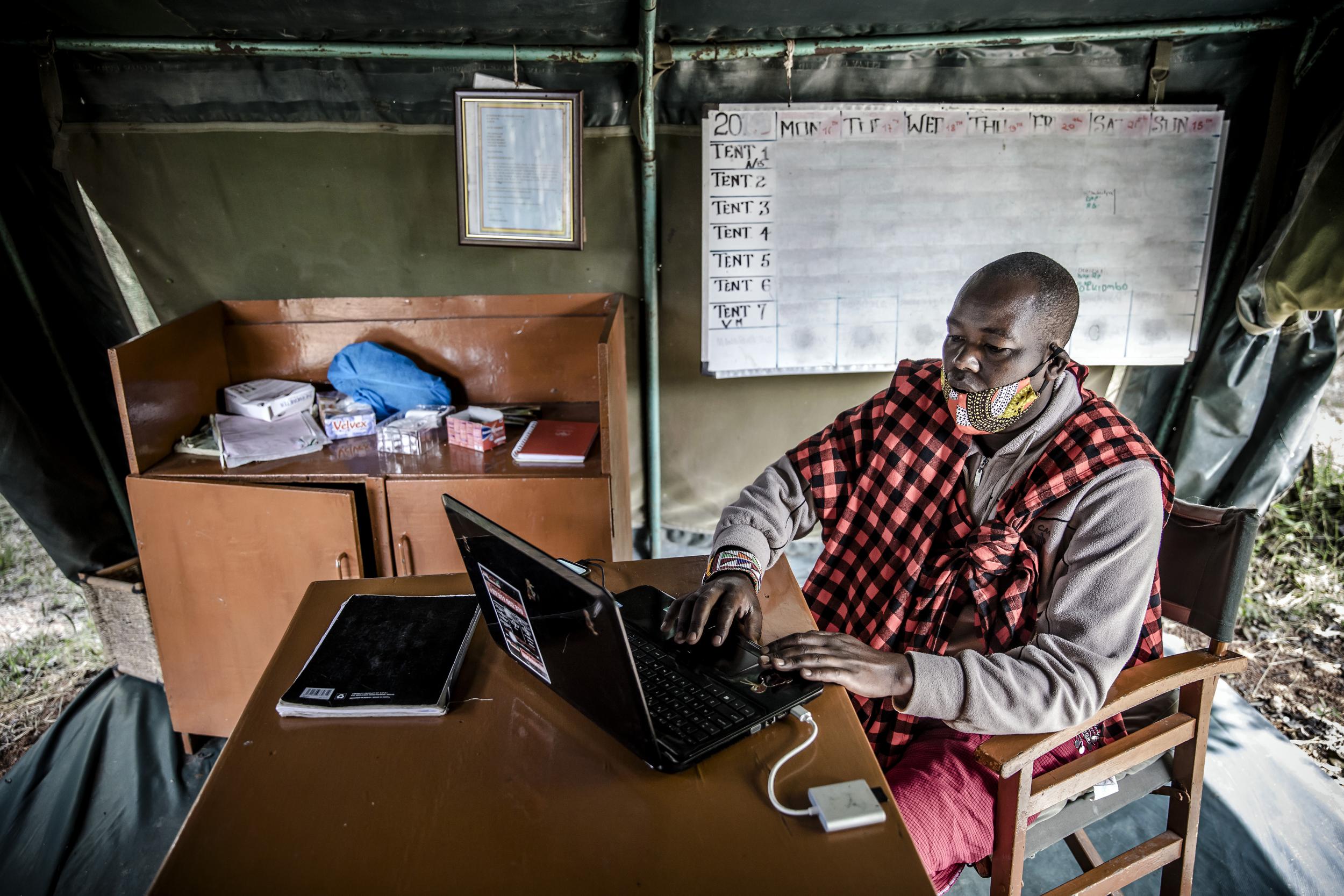 Jimmy Lemara at the Porini Mara Camp, where a blank board that would normally include a list of tourists hangs behind him