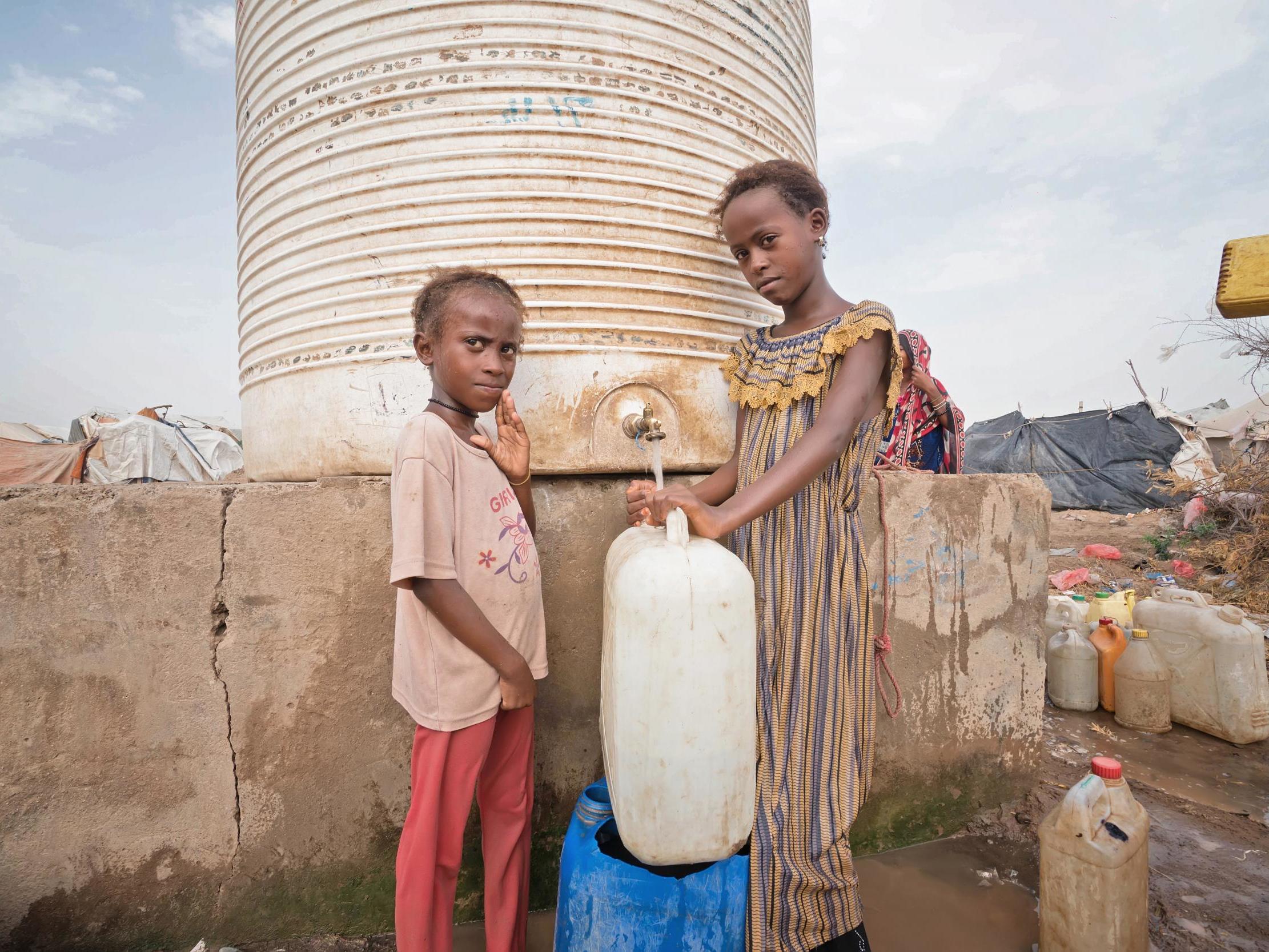 Two cousins collecting water from a storage tank in Al-Baytarah camp