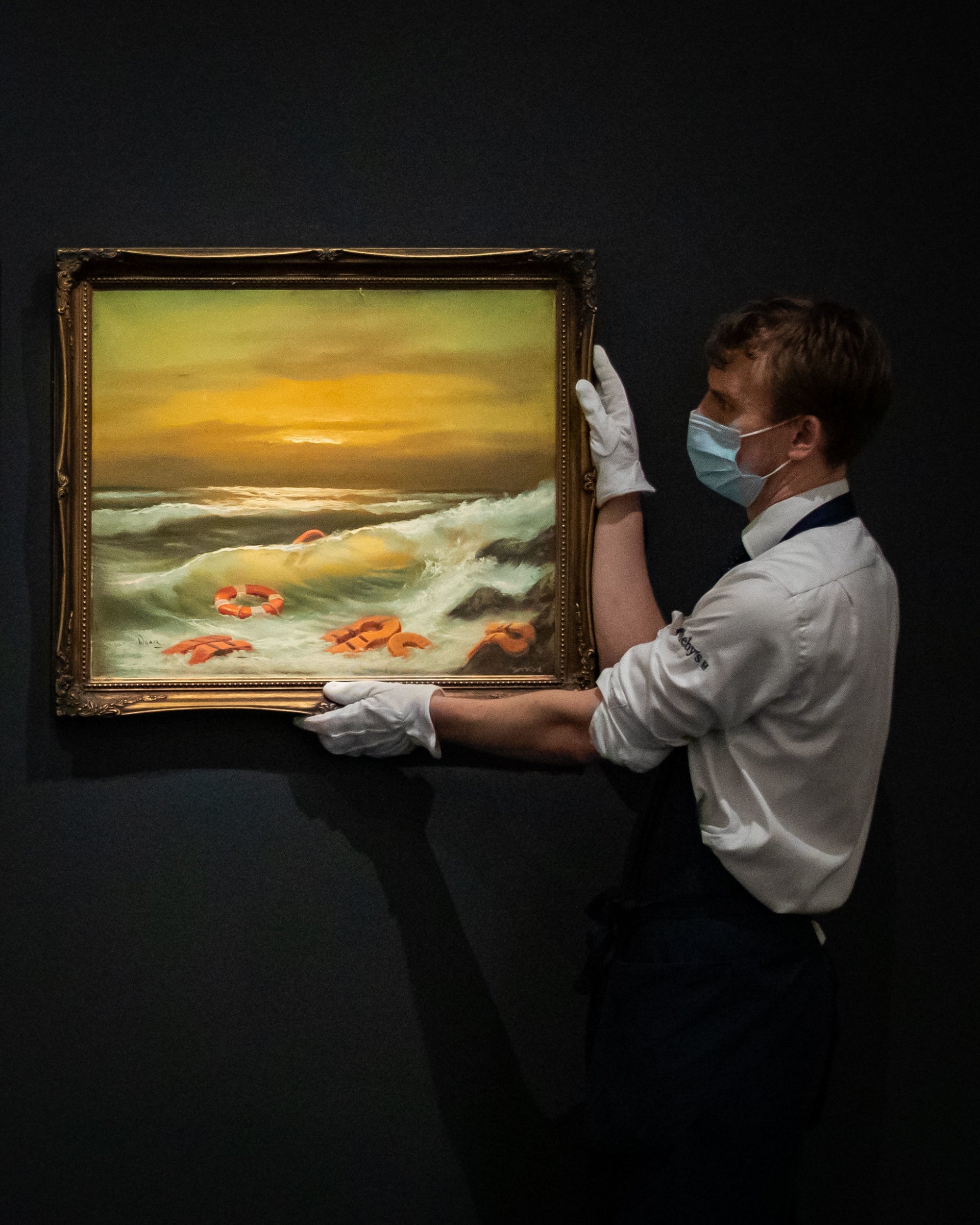 A gallery assistant holds one of a triptych, Mediterranean Sea View by Banksy