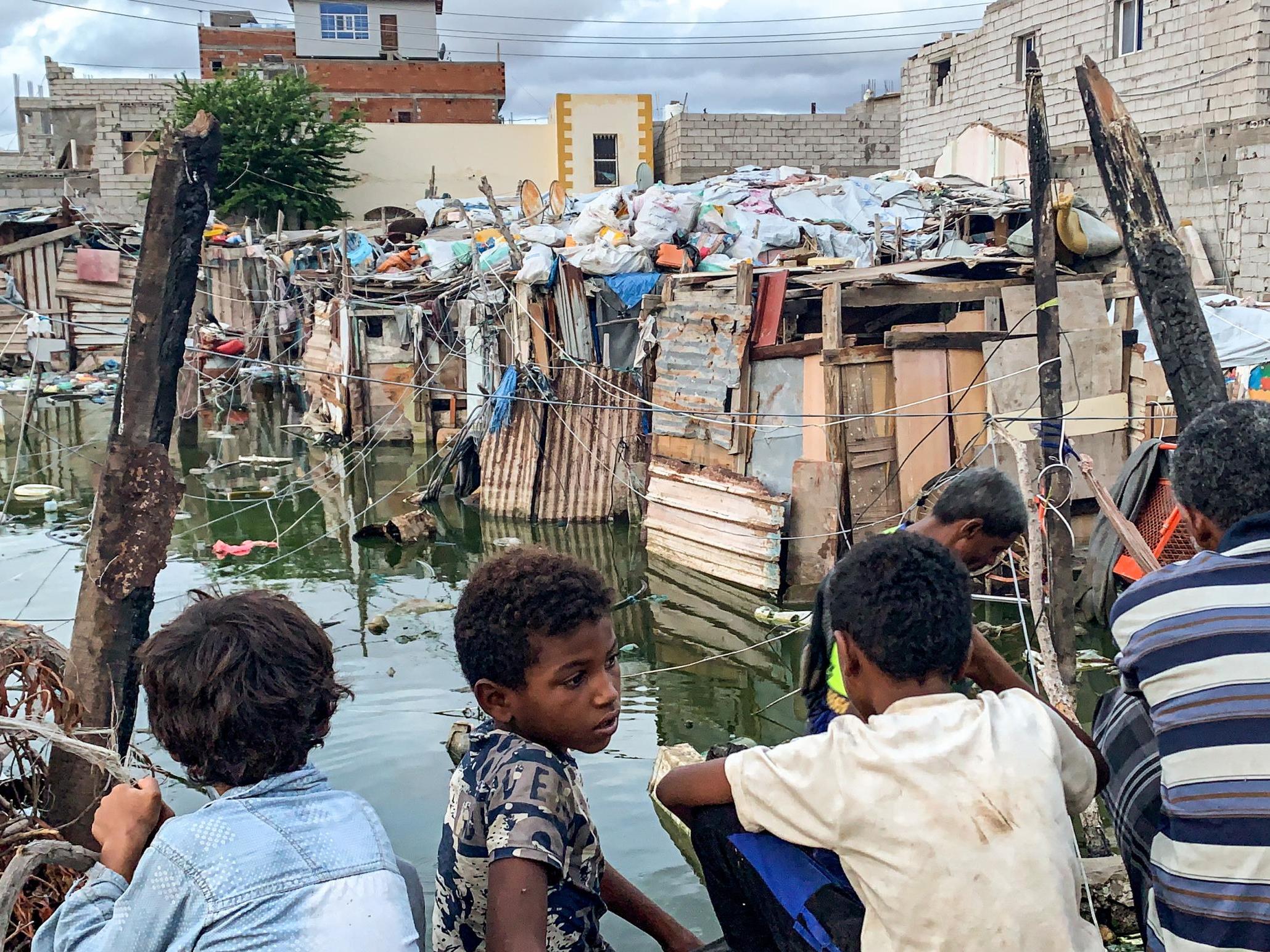 Children watch as workers prepare to drain sewage water from an Aden camp flooded by rainwater for Yemenis displaced by conflict from Taez, Ibb, and Hodeidah