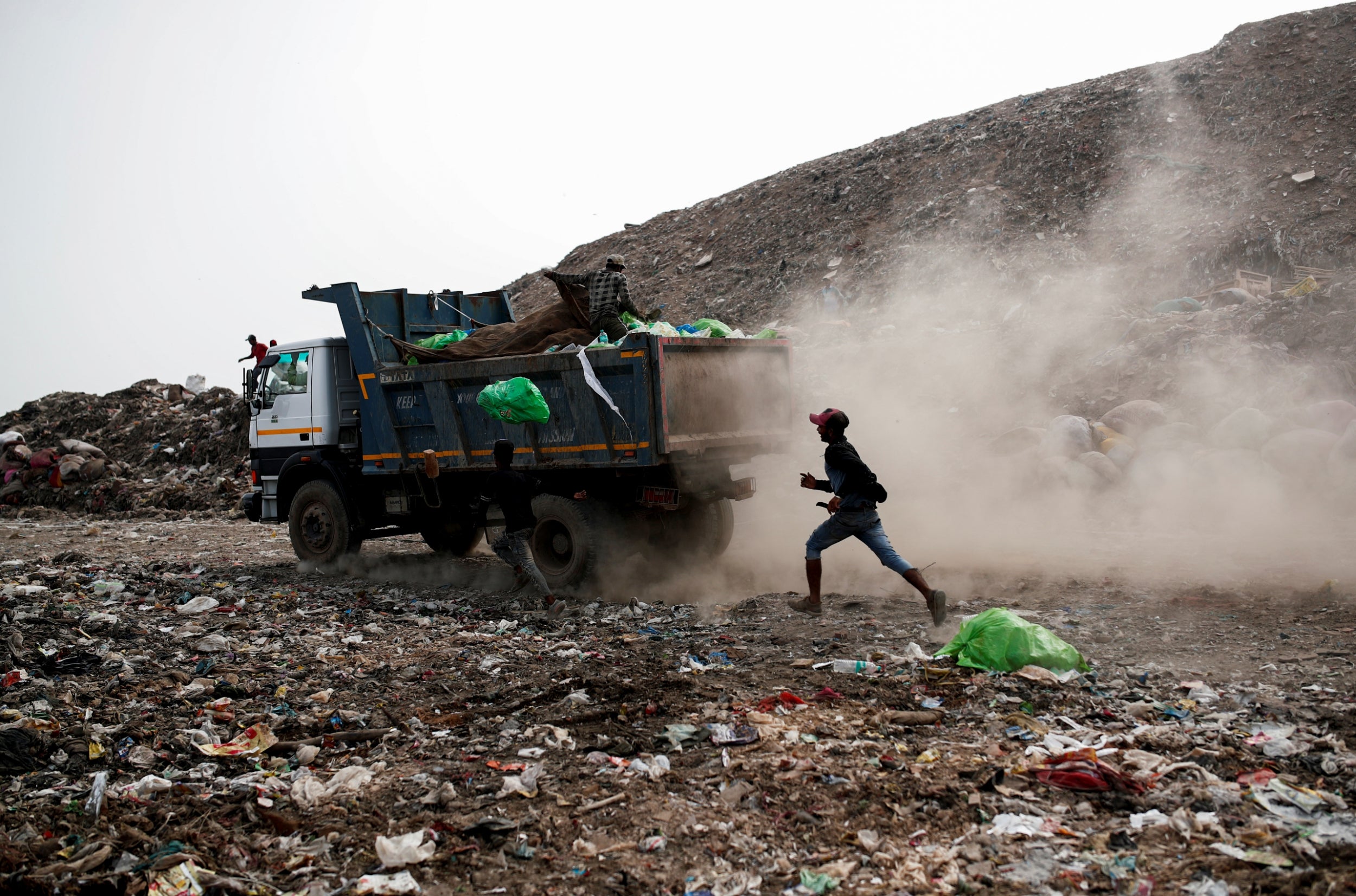 A waste collector runs behind a truck carrying rubbish