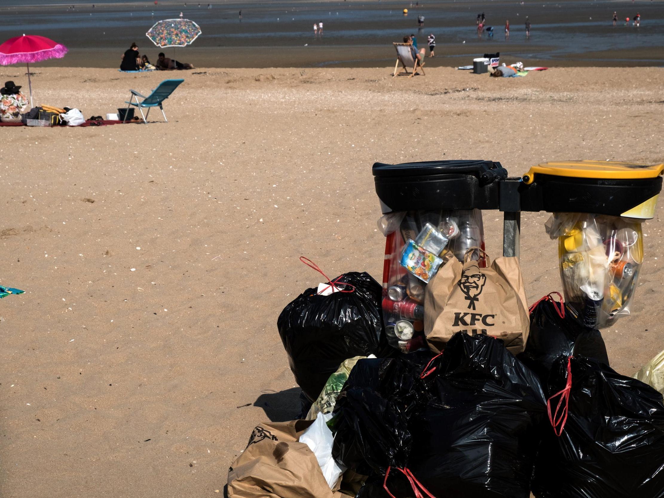 People enjoy the beach, next to a mountain of trash placed next to a bin, in Houlgate, northwestern France