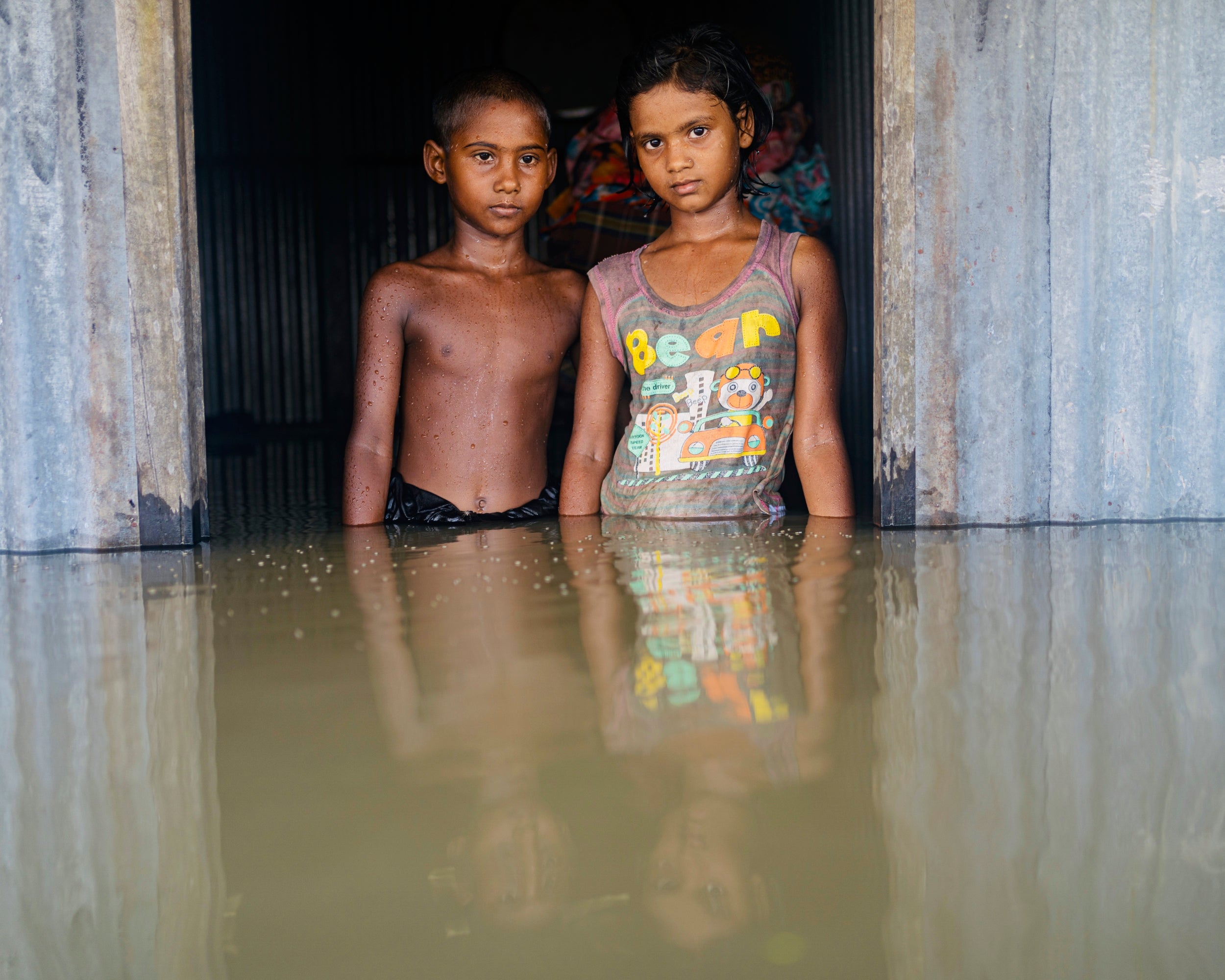 Sayma and Sumaiya Khatun standing on the doorstep of their submerged house