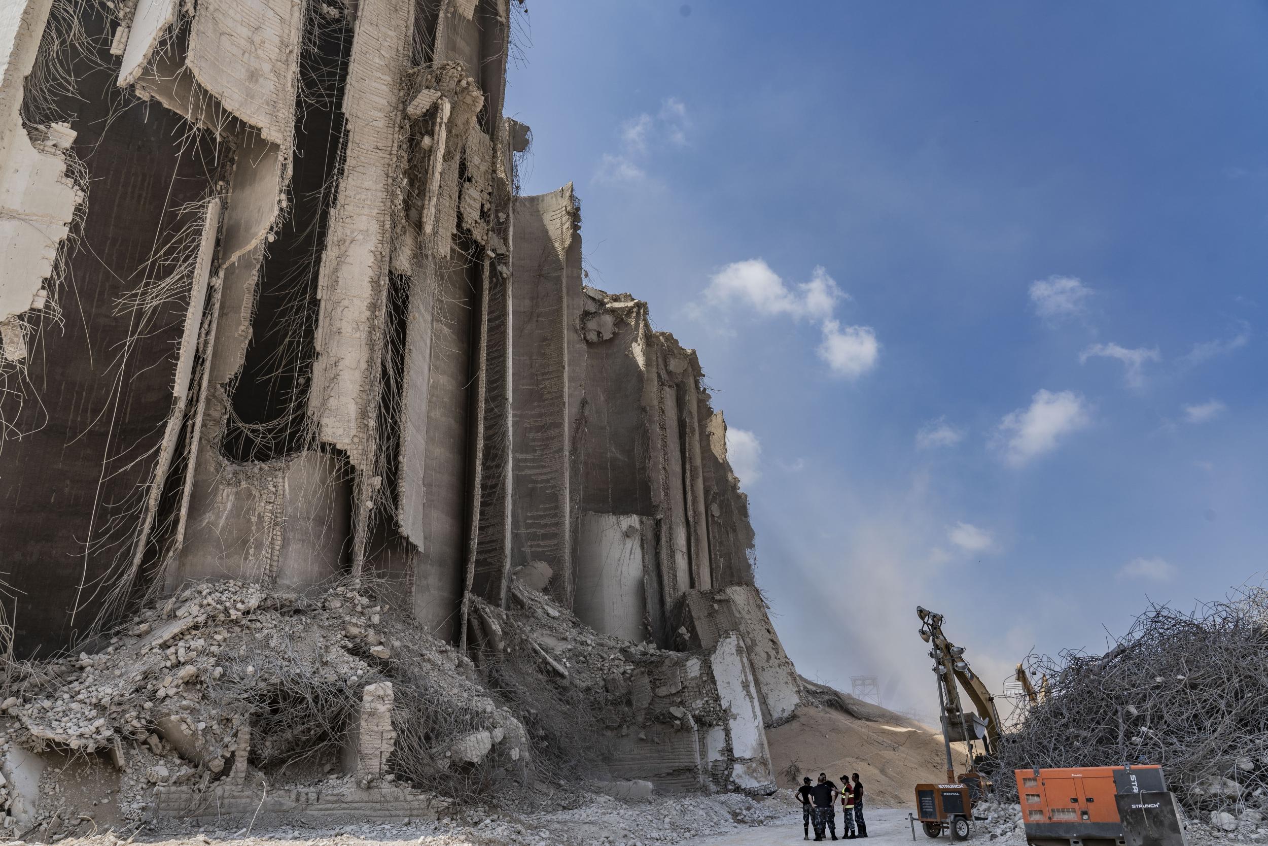 Firefighters stand in the shadow of Beirut's destroyed grain silo