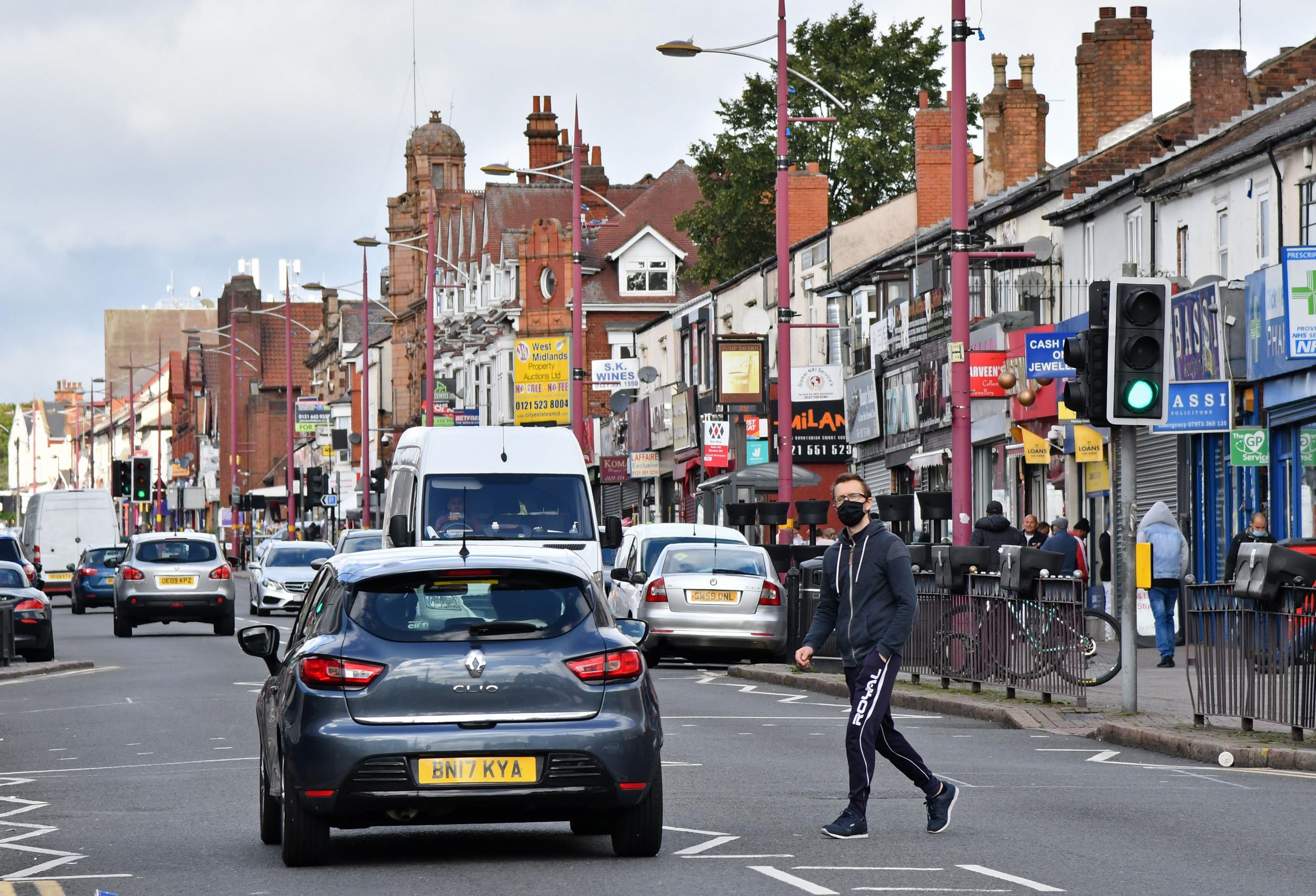 A man wearing a protective face mask crosses Soho Road in the Handsworth area of Birmingham