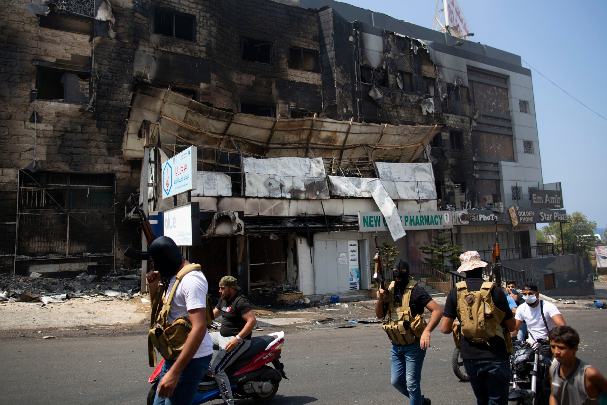Sunni gunmen walk in front of a building set on fire in Thursday night's clashes, during the funeral procession for Hassan Zaher Ghosn, 14