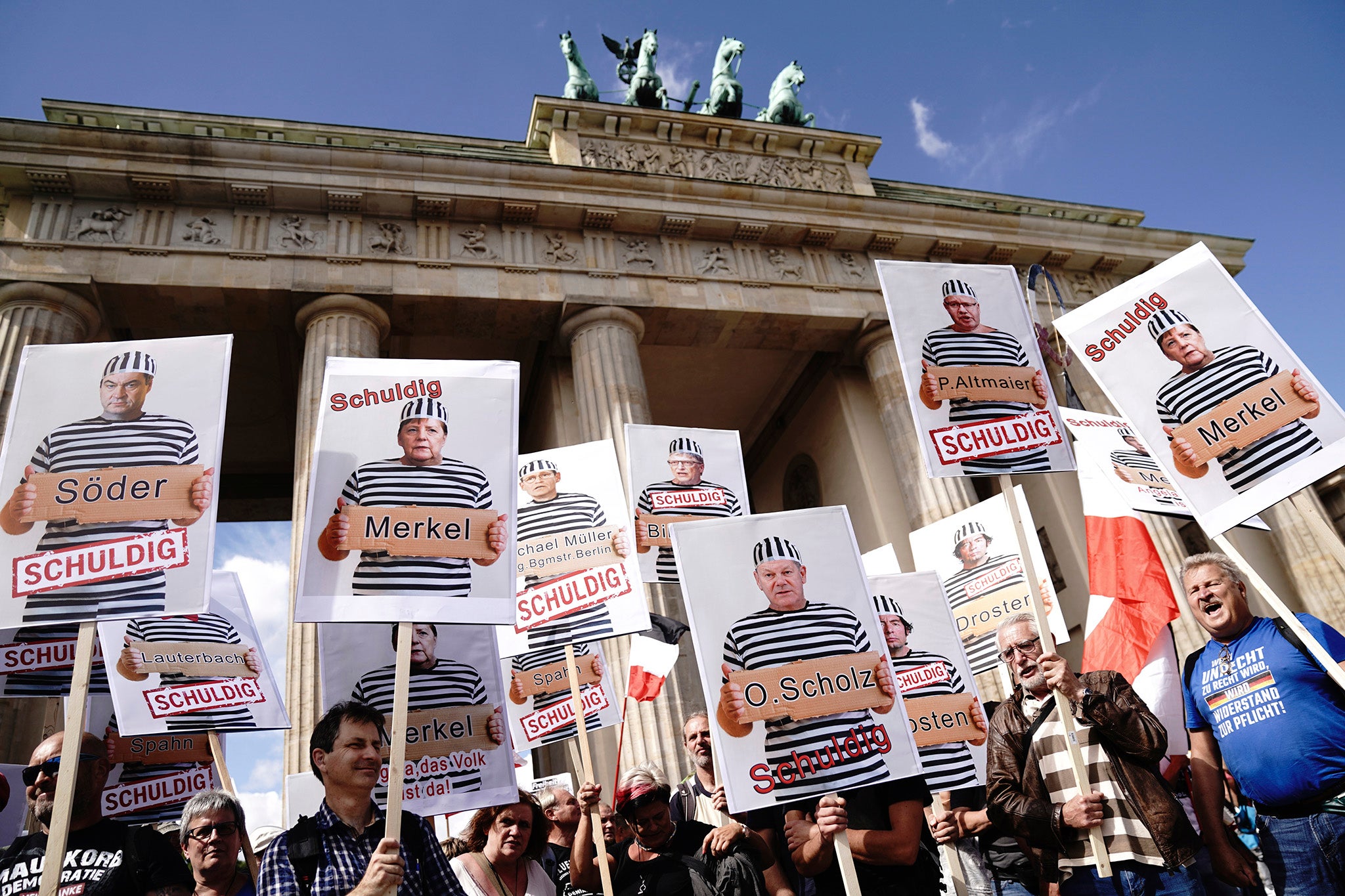 Demonstrators hold signs depicting various government figures and virus experts as prisoners