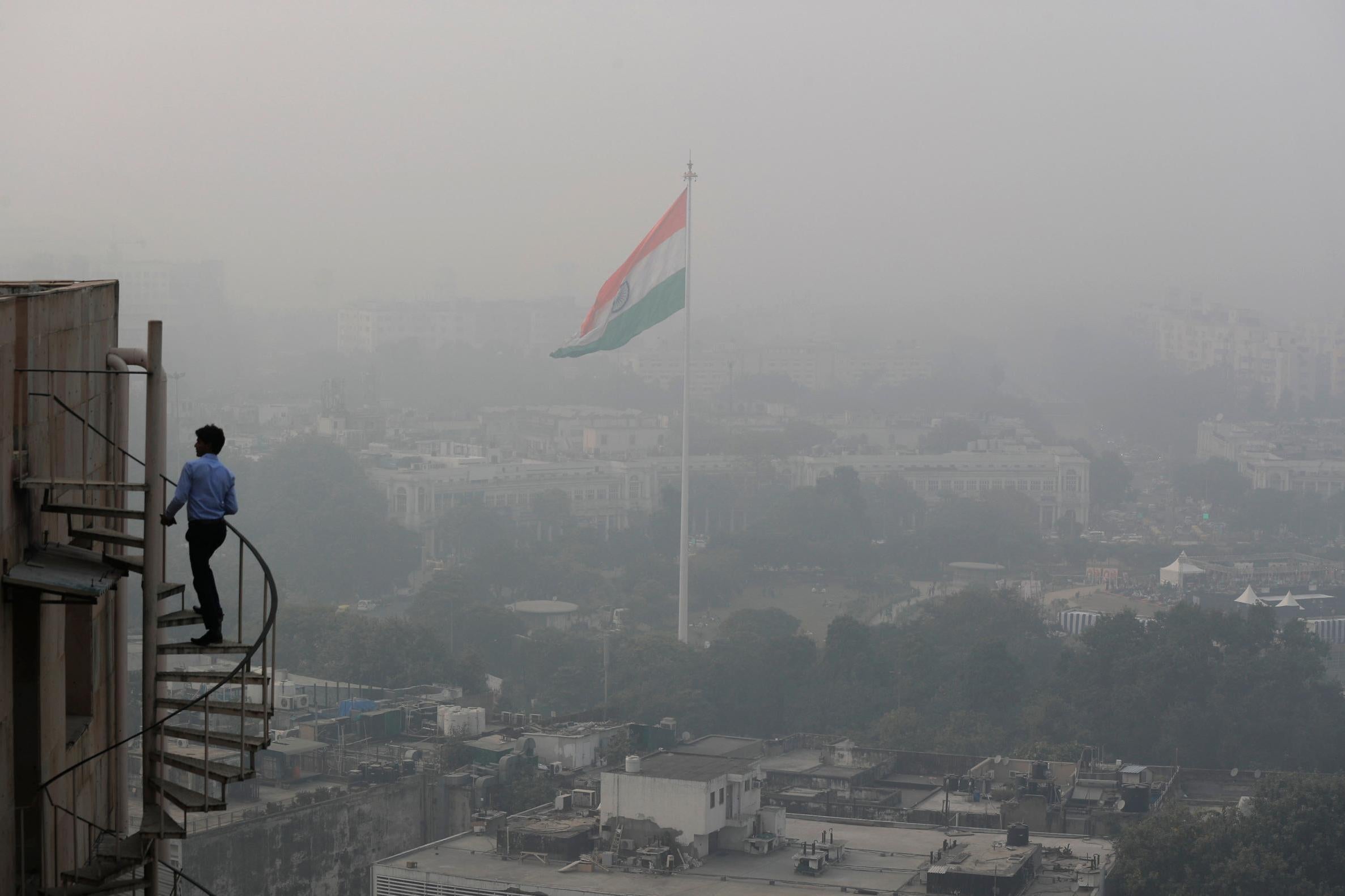 An Indian man walks up stairs as Delhi’s skyline is seen enveloped in smog and dust